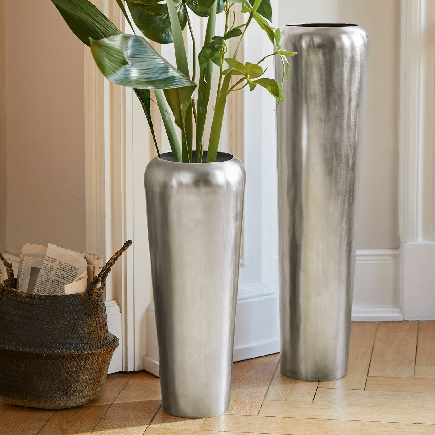 Bodenvase 2er Set Carolan Zwei hohe silberne Metallvasen auf dem Boden in einem hellen Raum mit grünen Pflanzen