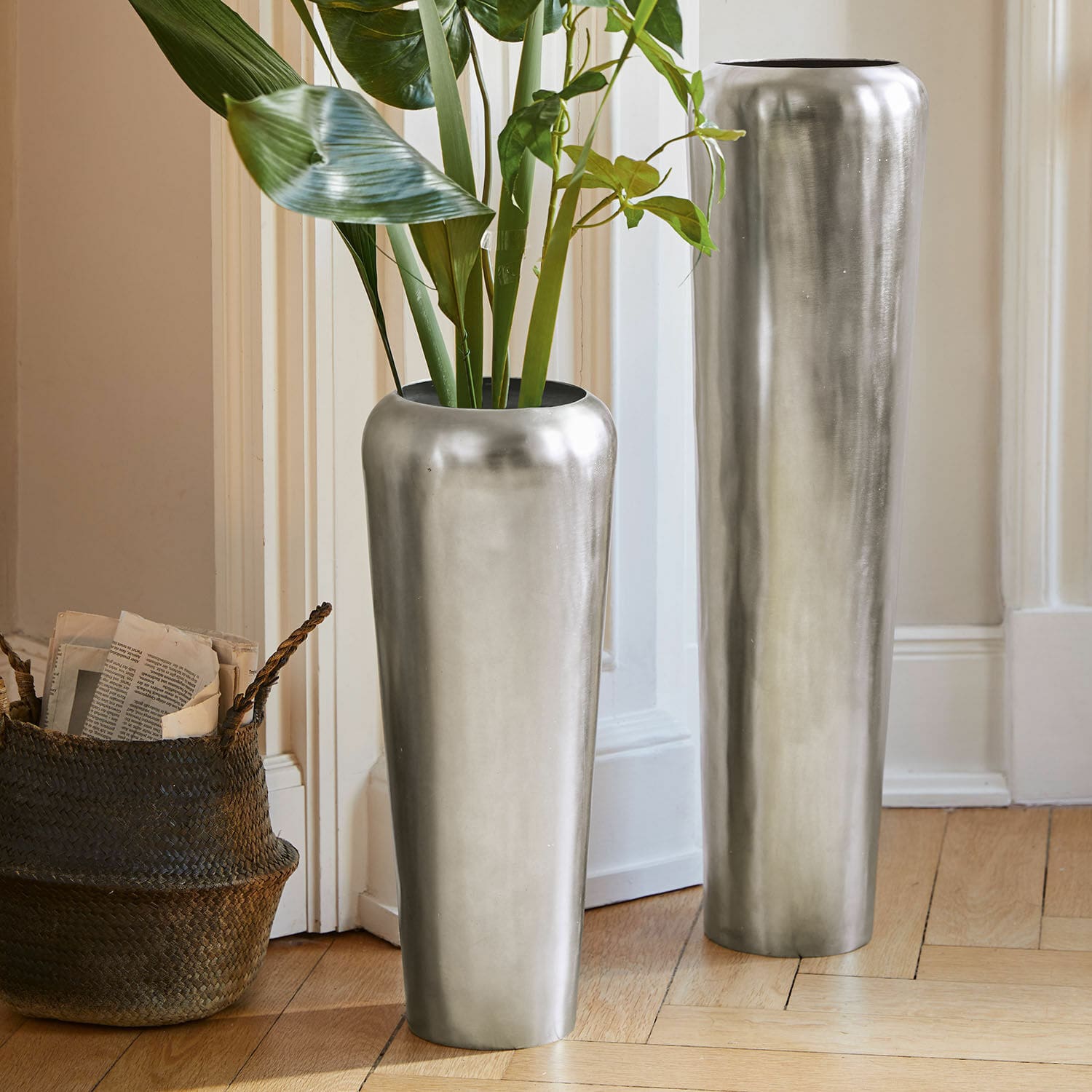 Bodenvase 2er Set Carolan Zwei hohe silberne Metallvasen auf dem Boden in einem hellen Raum mit grünen Pflanzen