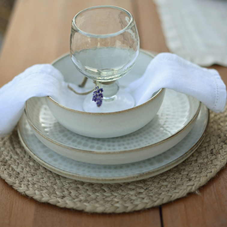 Set aus weisser Keramik mit Tellern und Schale auf geflochtenem Platzset mit weisser Serviette