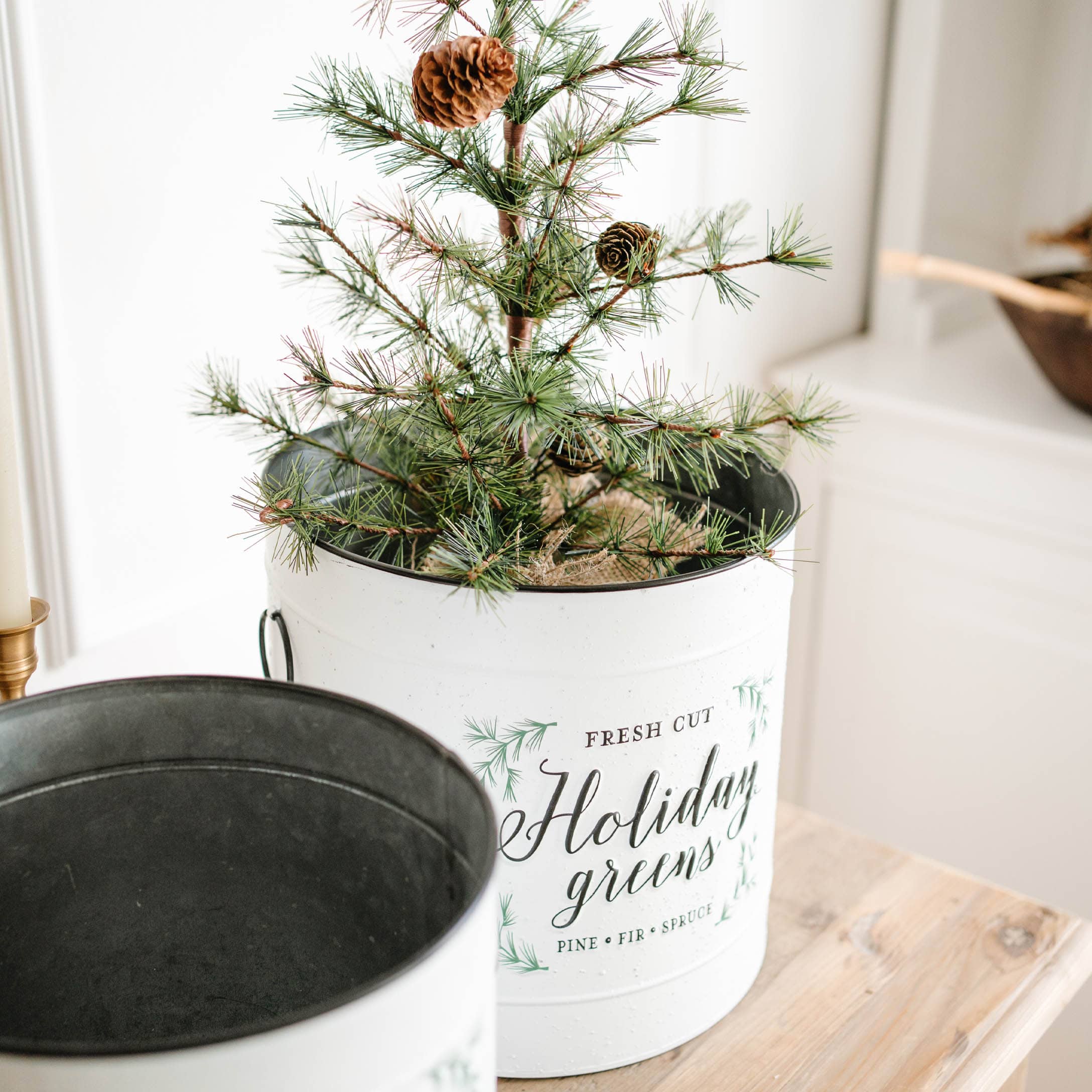 Weisse Metallpflanzschale mit grünen Kiefernzweigen und Zapfen auf Holztisch