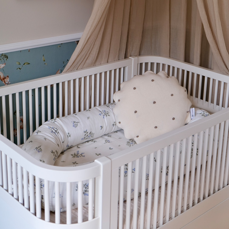 Weisses Babybett mit weichem Kissen und floralem Bettzeug in Pastellfarben