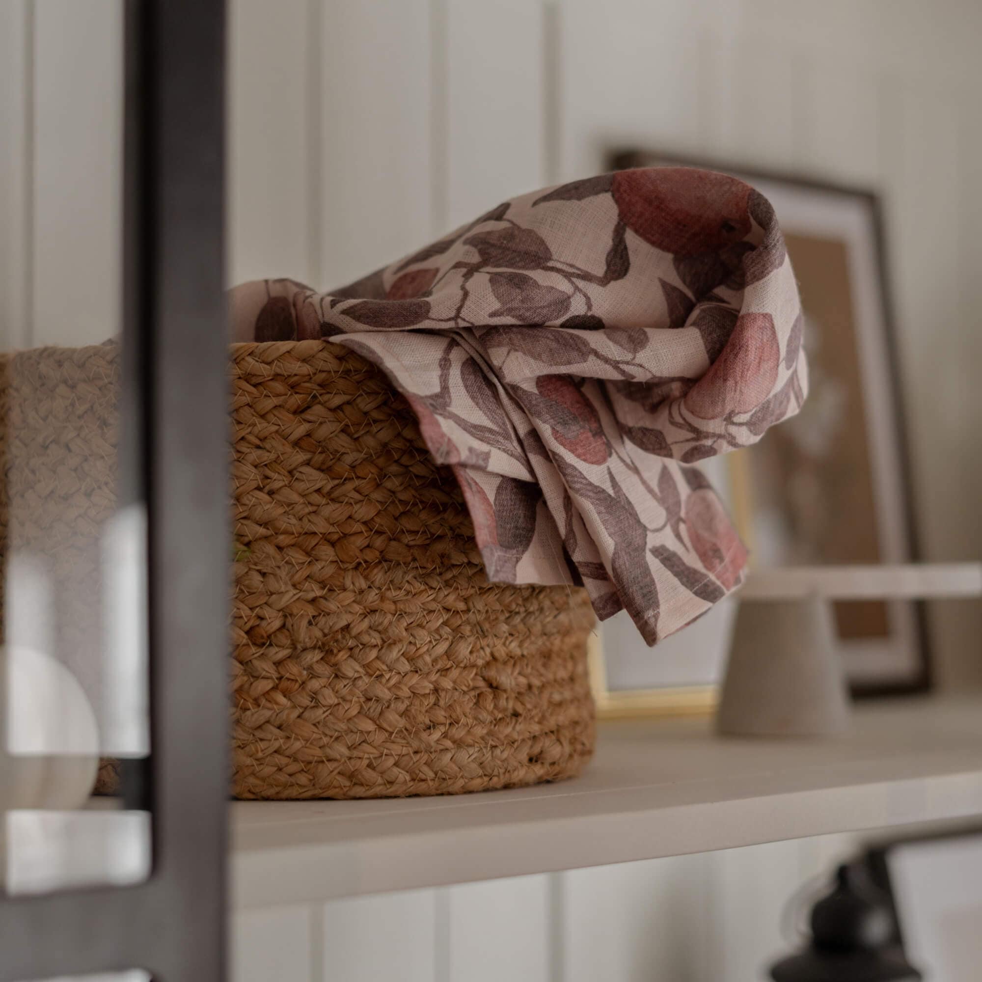 Geflochtener Naturkorb mit Leinenstoff in rosa-braunem Blumenmuster auf weissem Regal