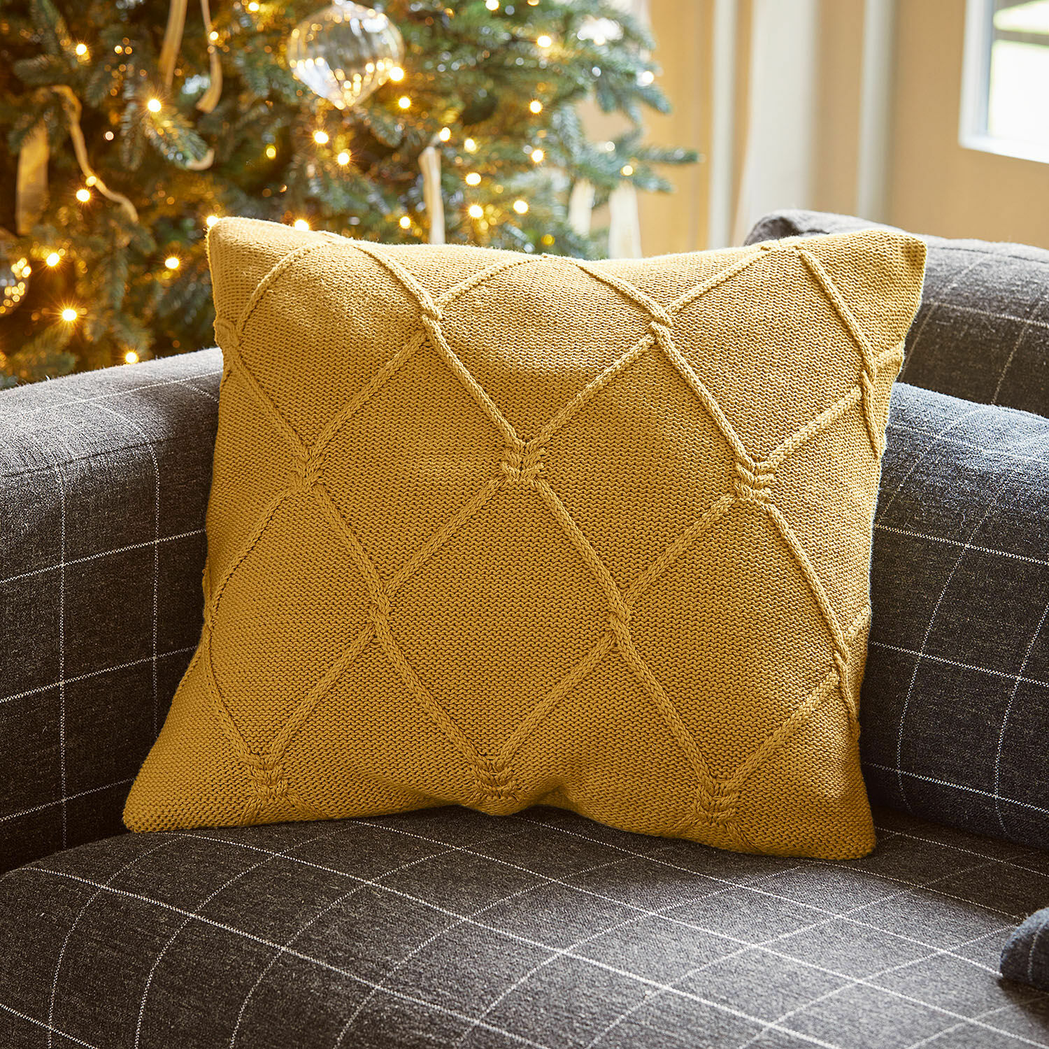 Kissenhülle Cresil Senfgelbe Strickkissen auf grauem Sofa mit Karomuster für ein gemütliches Wohnzimmer