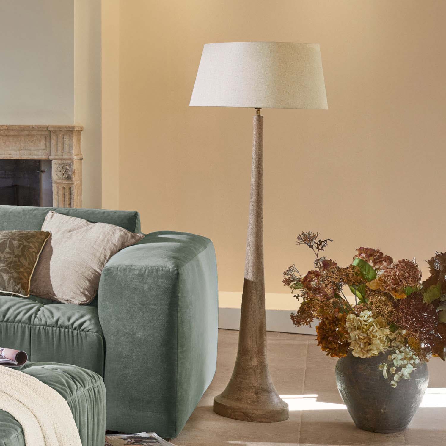 Stehlampe mit Holzsockel und beigem Schirm in modernem Wohnzimmer mit grünem Sofa