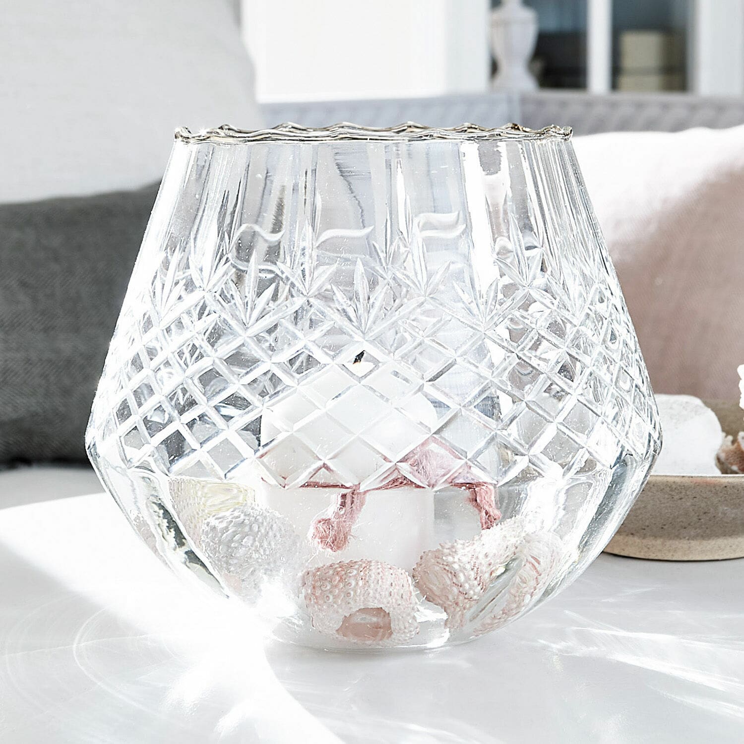 Windlicht Tianie Glas-Teelichthalter mit graviertem Muster, weisser Kerze und Muscheldekor auf dem Tisch