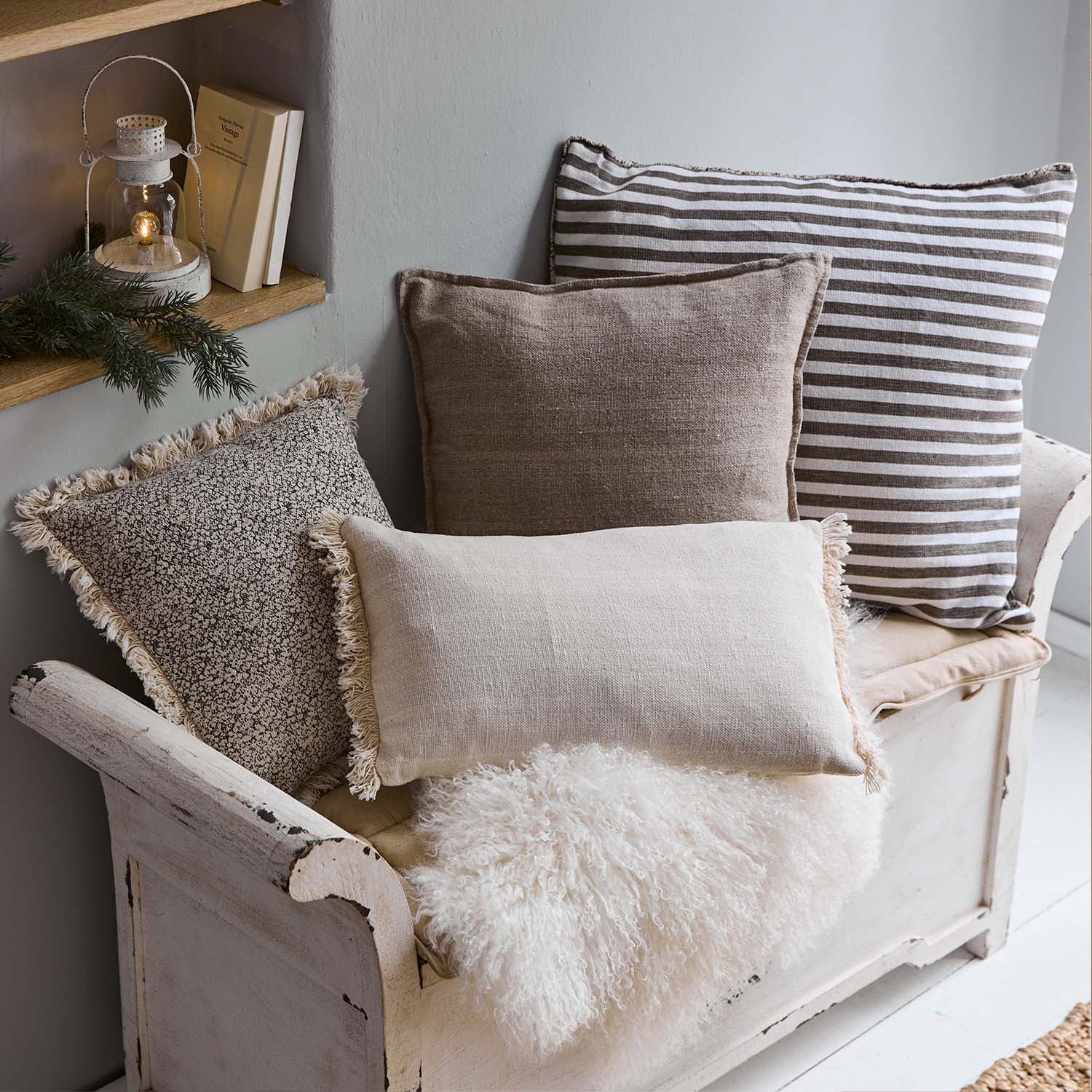 Set dekorative Kissen in Beige- und Brauntönen auf weisser Holzbank mit flauschiger Decke