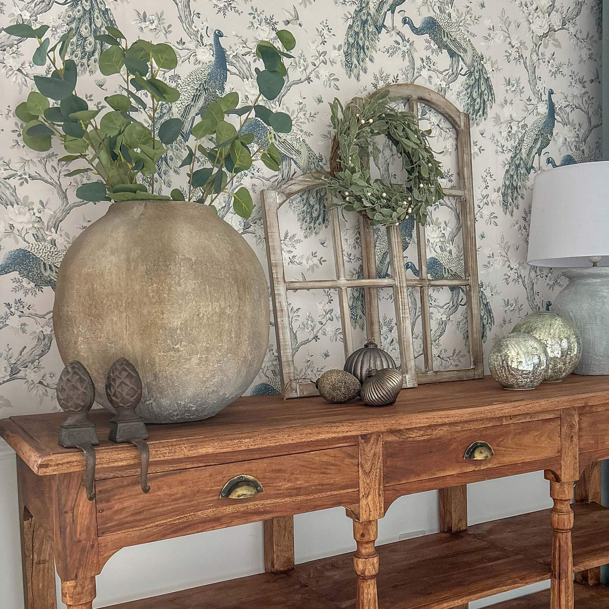 Holztisch mit grosser Tonvase, grünen Blättern, Lampe und dekorativen Accessoires darauf