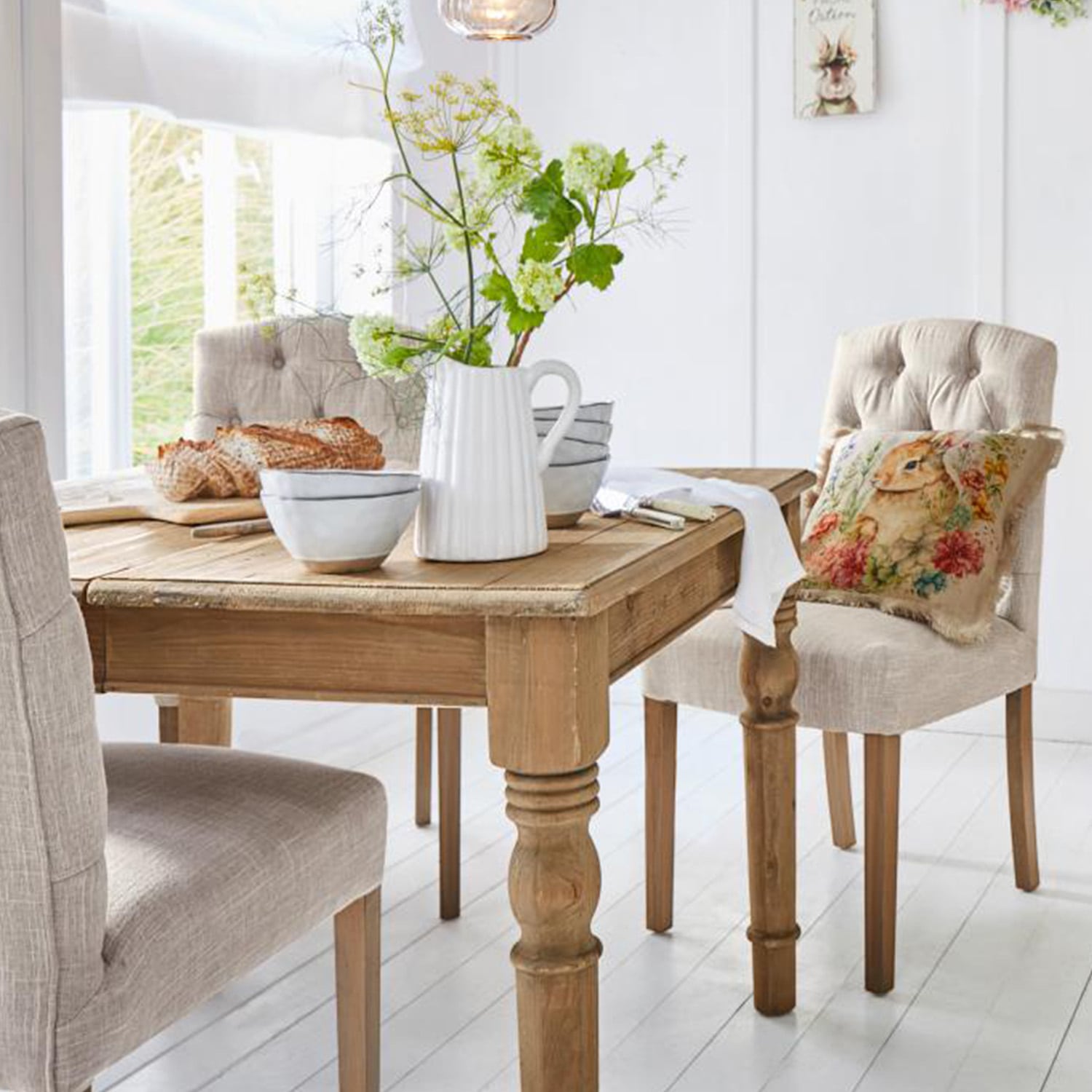 Heller Holztisch mit dekorativem Krug und Schalen, beige gepolsterte Stühle in hellem Esszimmer