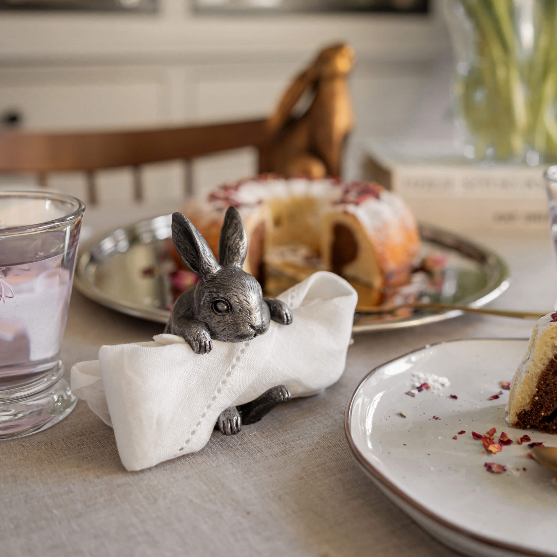 Metall-Serviettenhalter in Hasenform auf Tisch mit Kuchen und Wasserglas