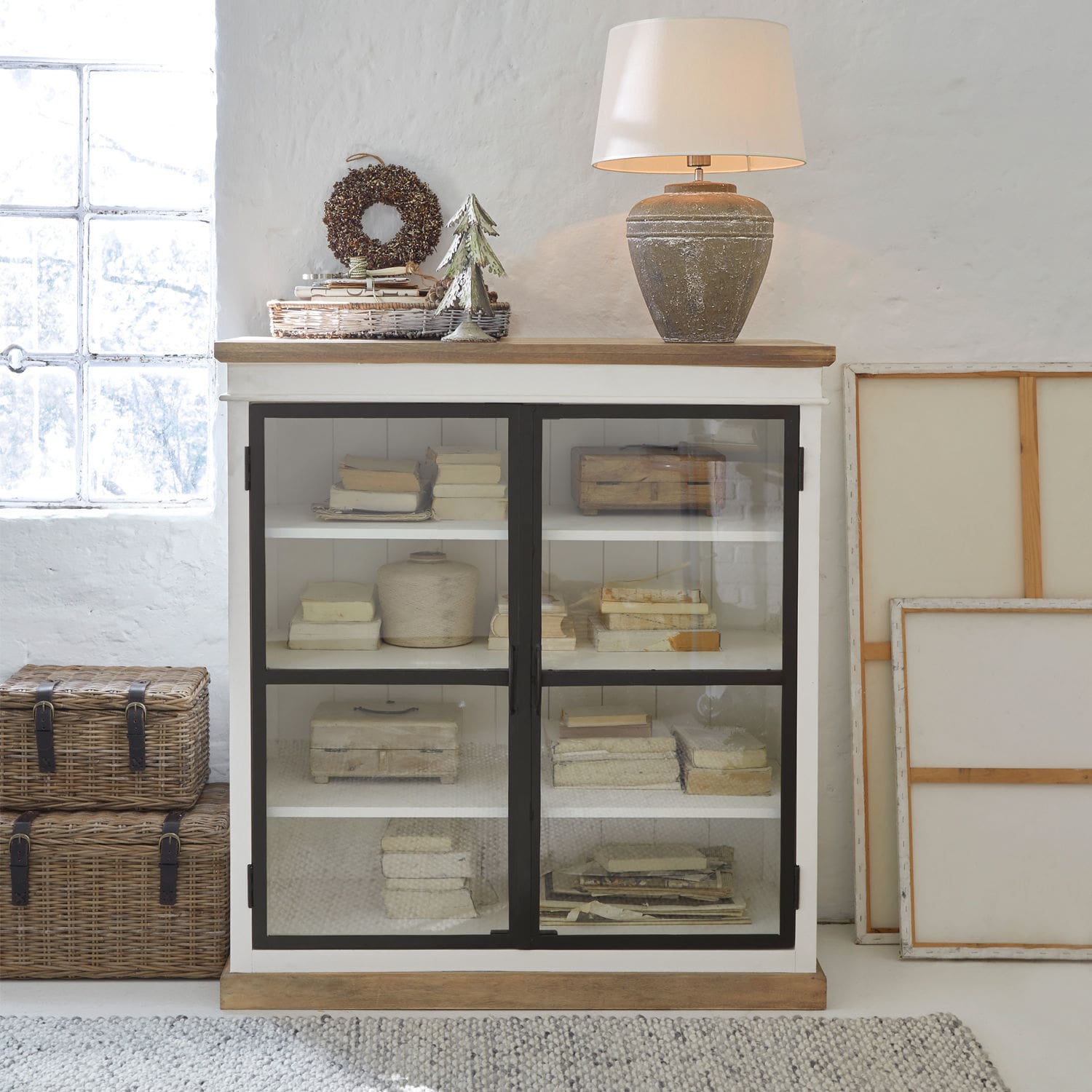 Weisse Holzvitrine mit Glastüren und Keramiklampe im Vintage-Stil auf der Ablage