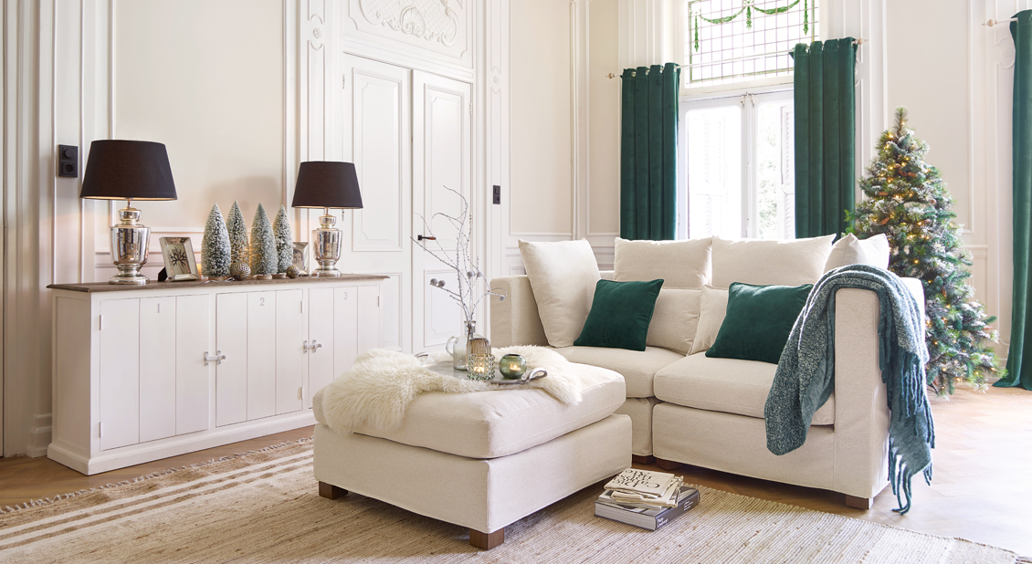 Gemütliches Wohnzimmer mit beigem Sofa, grünen Kissen und geschmücktem Christbaum, Winterdekoration