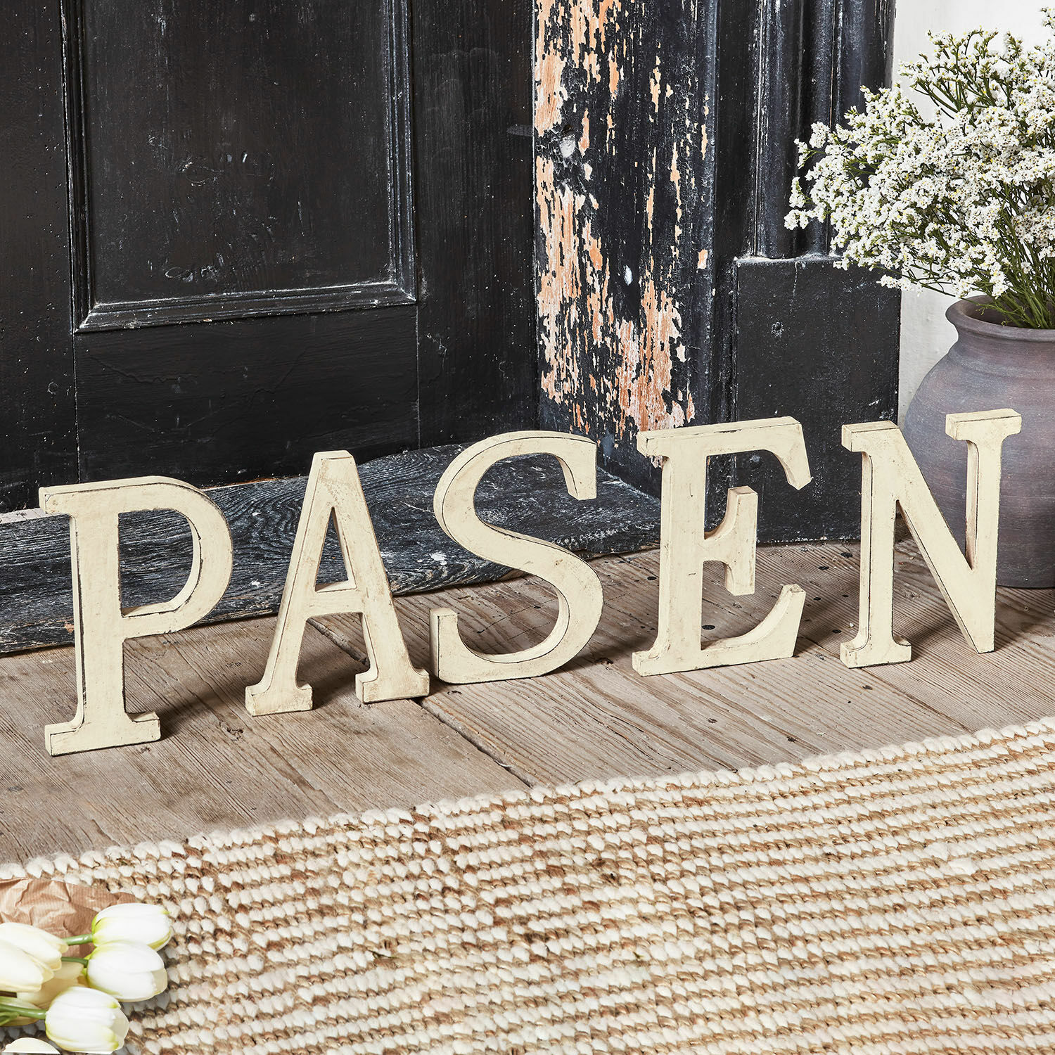 Dekorative, cremefarbene Holzbuchstaben bilden das Wort PASEN auf rustikalem Holzboden.