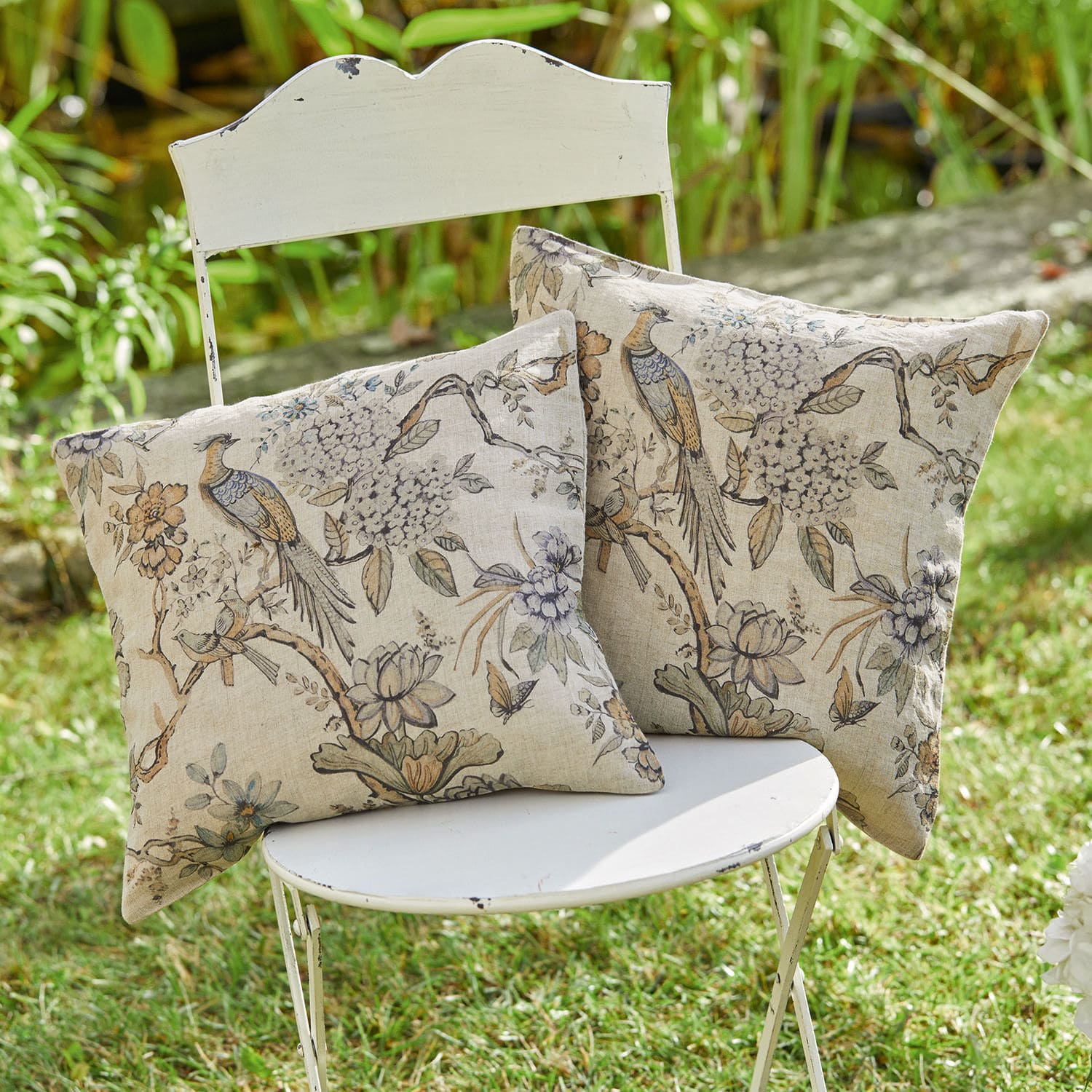 Kissenhülle 2er Set Lorry Zwei dekorative Baumwollkissen in Beige mit Vogel- und Blumenmuster auf weissem Stuhl im Garten