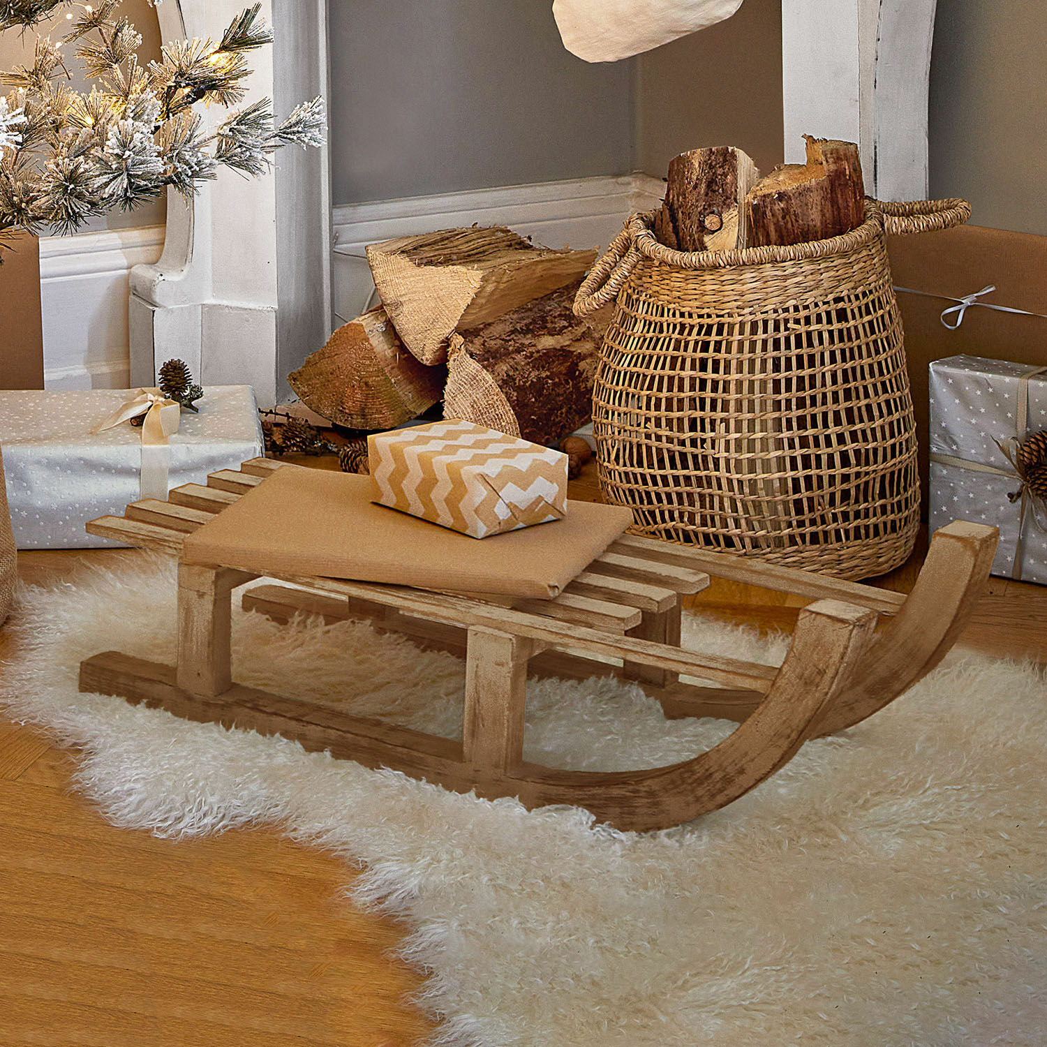 Deko-Schlitten FSC®-100% Hoekstra Dekorativer Holzschlitten auf weissem Fellteppich mit Geschenken und Korb mit Holzscheiten