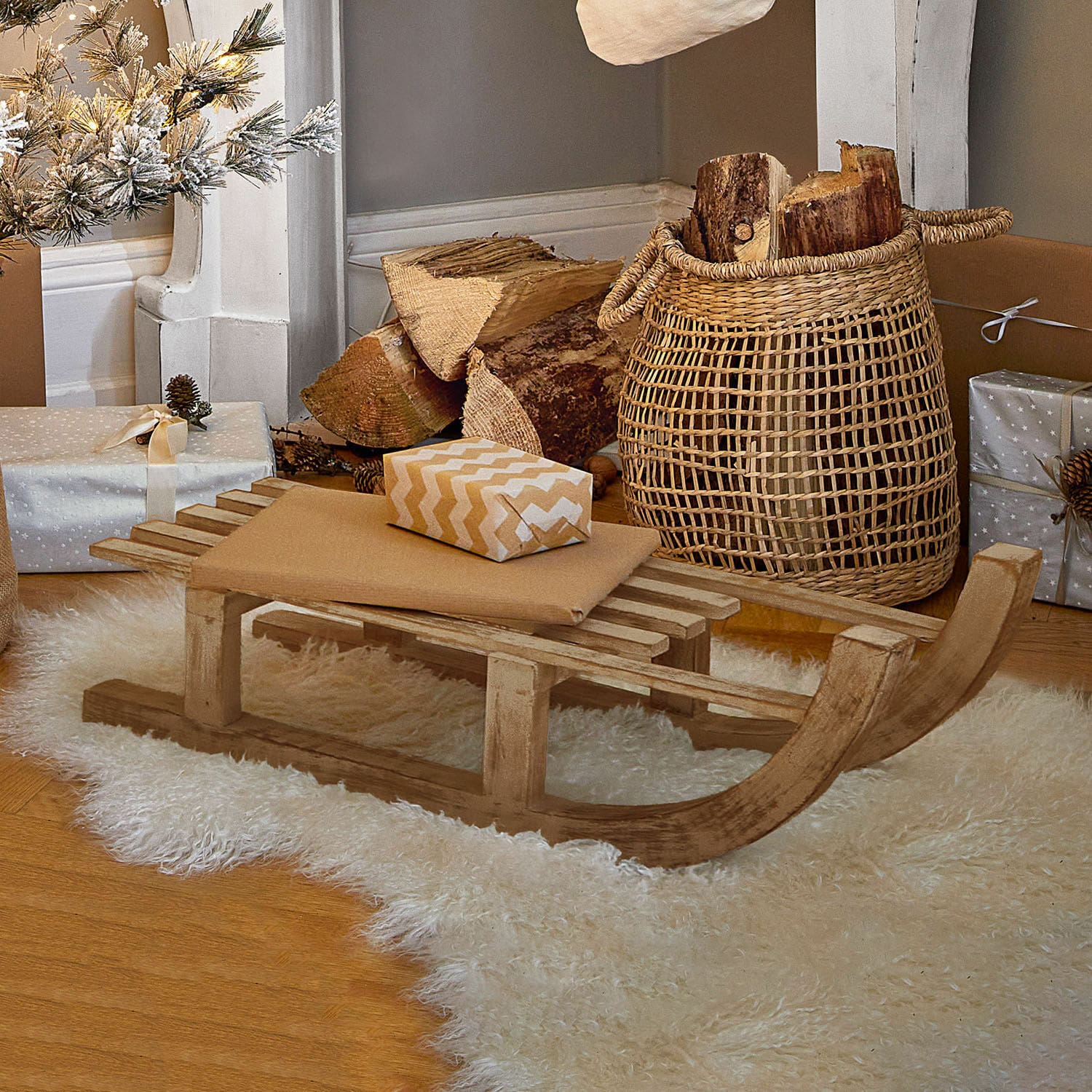Deko-Schlitten FSC®-100% Hoekstra Dekorativer Holzschlitten auf weissem Fellteppich mit Geschenken und Korb mit Holzscheiten