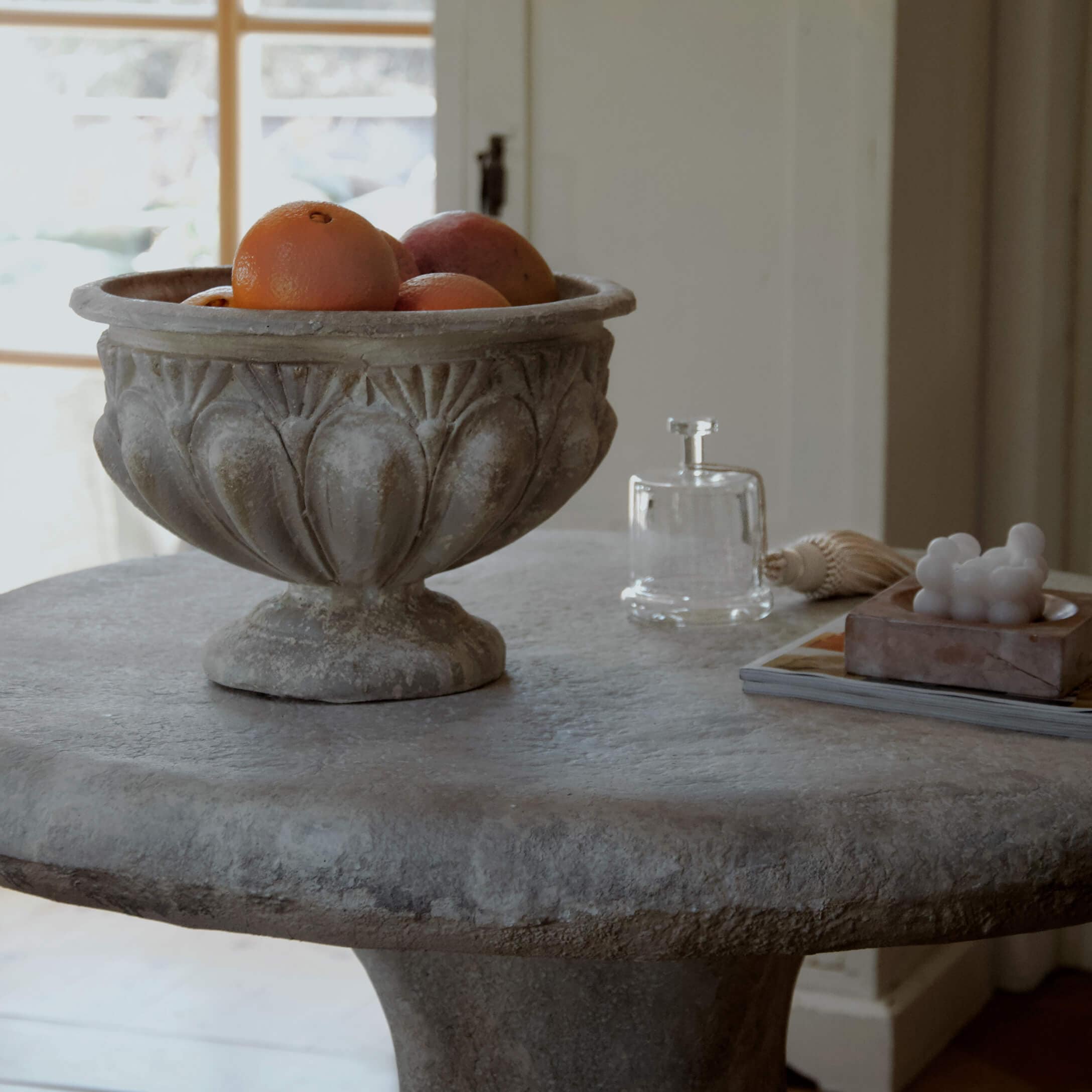 Dekorative Steinschale mit Orangen auf Steintisch in hellem Raum