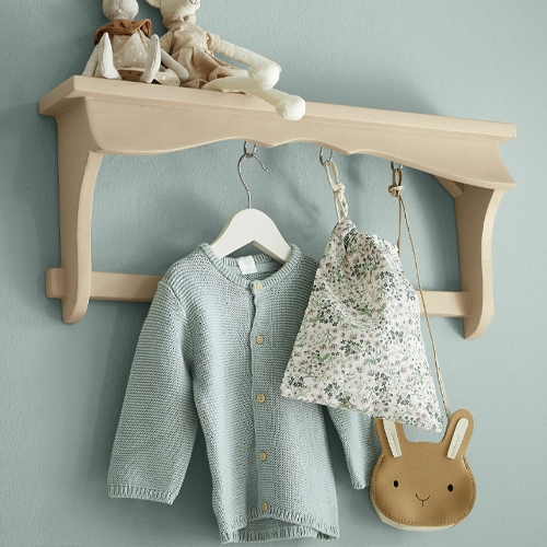 Beige Holz-Wandregal mit Haken, an dem ein hellblauer Pullover und eine Tasche mit Blumenmuster hängen