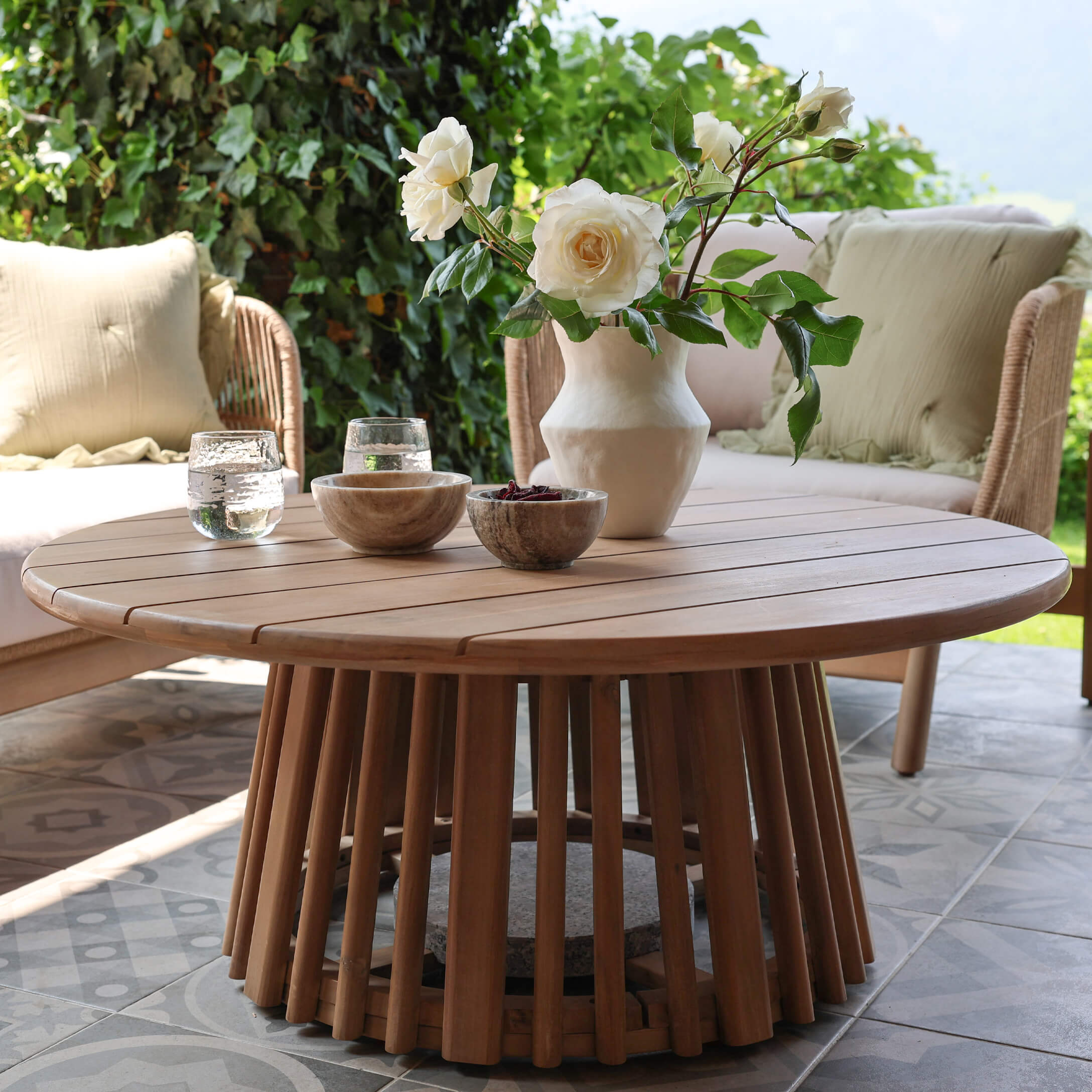Runder Couchtisch aus Teakholz in Naturfarbe auf der Terrasse mit Blumendekor und Steinschalen