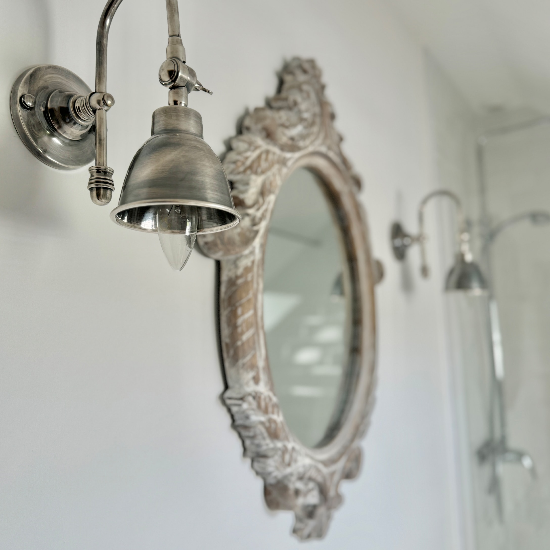 Vintage Metall-Wandleuchte im Badezimmer mit verziertem Holzrahmen-Spiegel an weisser Wand