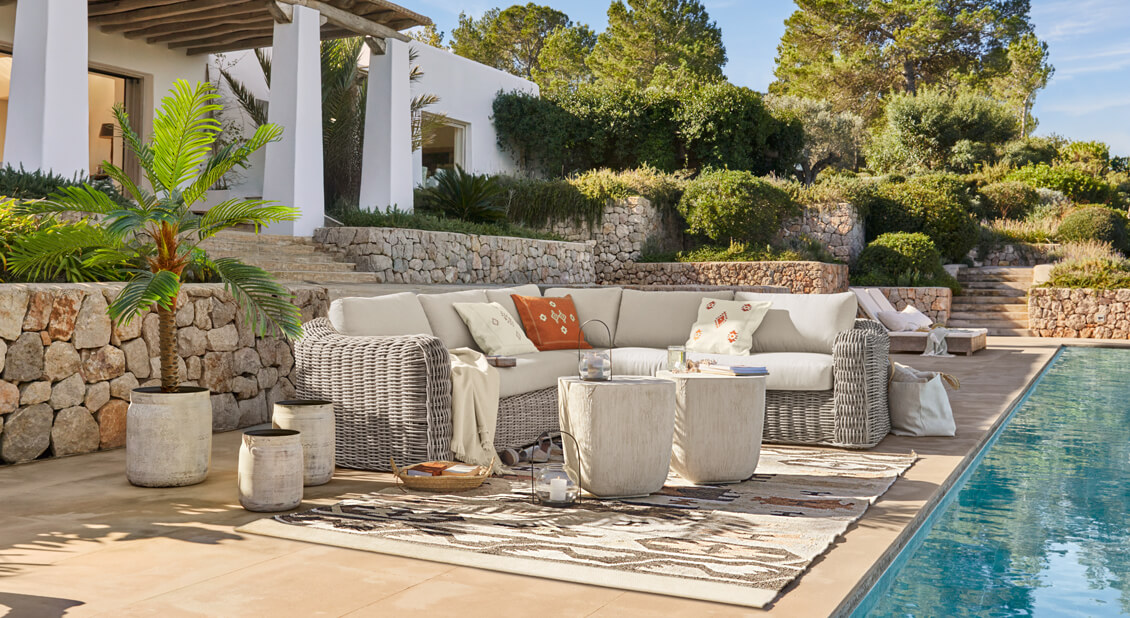 Gemütliche Ecklounge aus hellgrauem Rattan mit cremefarbenen Kissen am Pool im mediterranen Stil