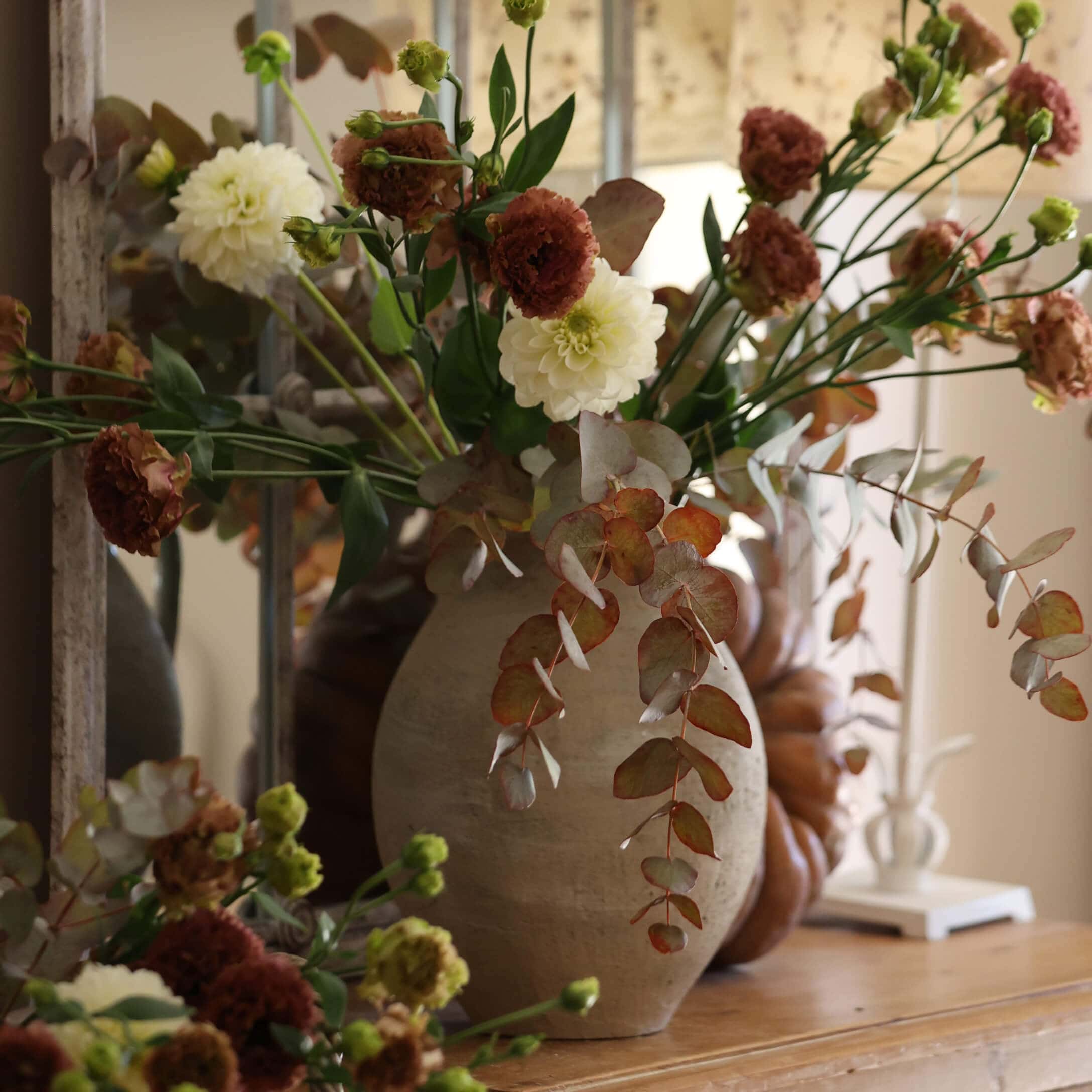 Beige Keramikvase mit weiss-braunem Blumenstrauss auf dekorativem Holztisch