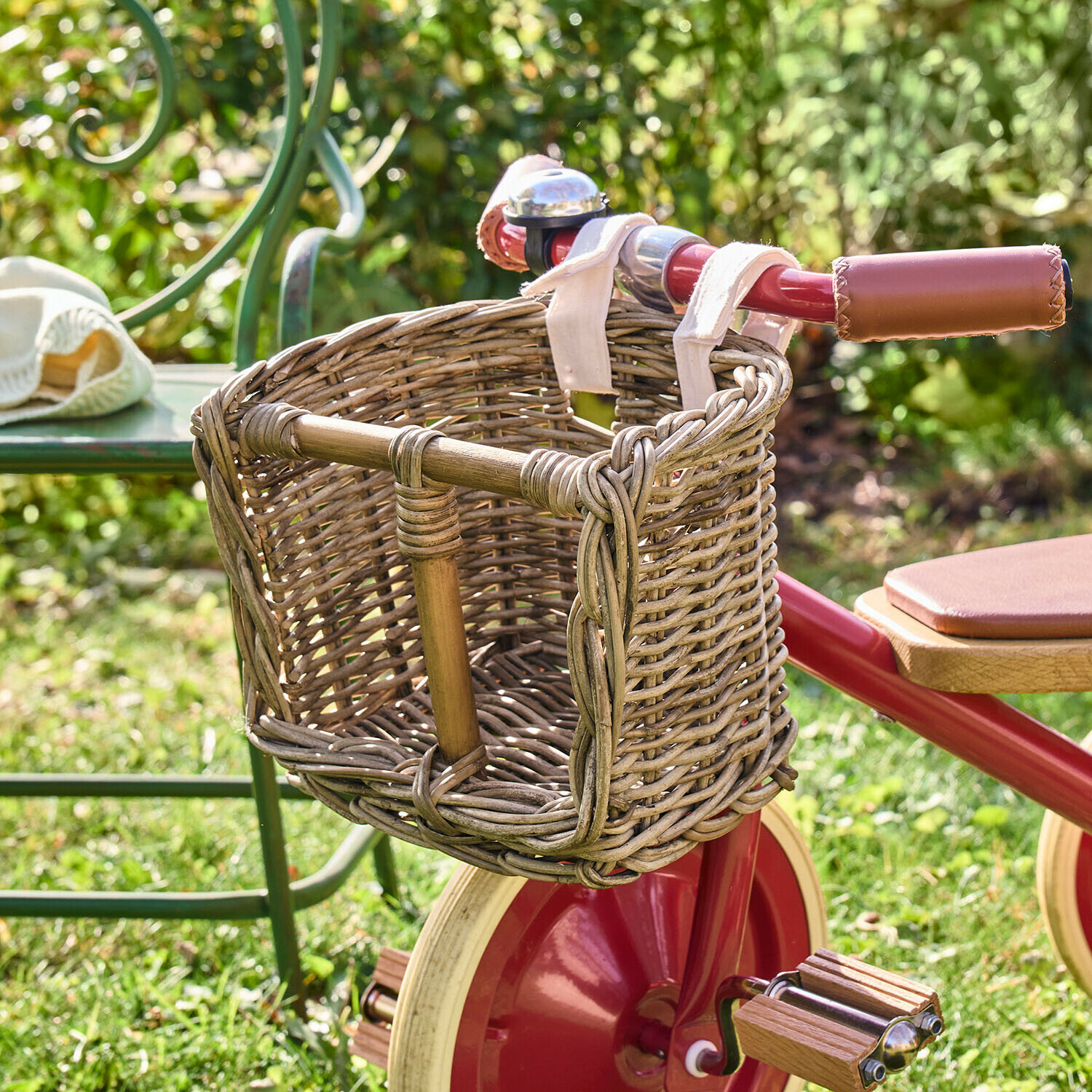 Puppenfahrradkorb Snokki Geflochtener Weidenkorb am roten Kinderfahrrad mit Ledergriffen, auf Gras im Garten