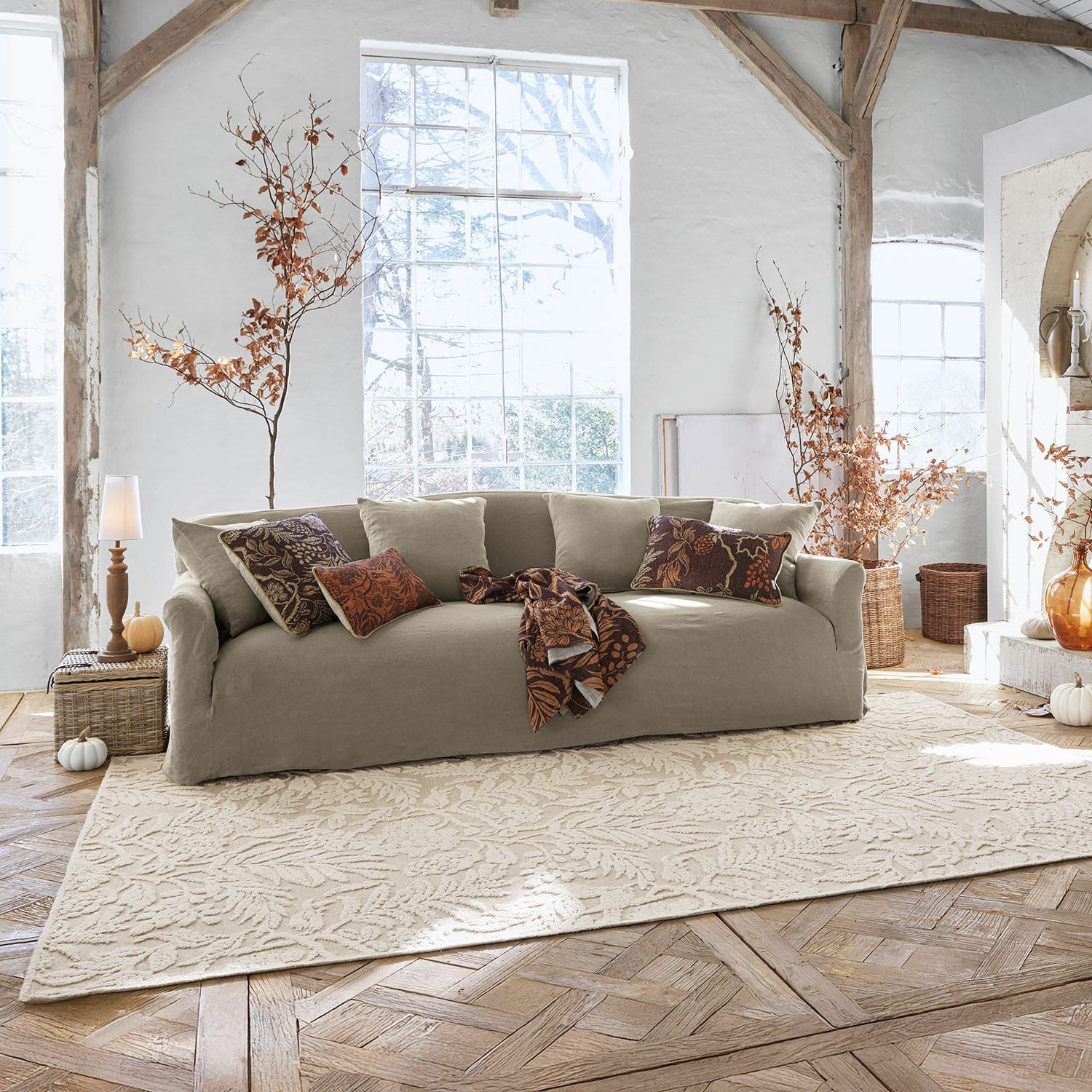 Beiges Stoffsofa im hellen Wohnzimmer mit dekorativen Kissen und gemustertem Blätterteppich