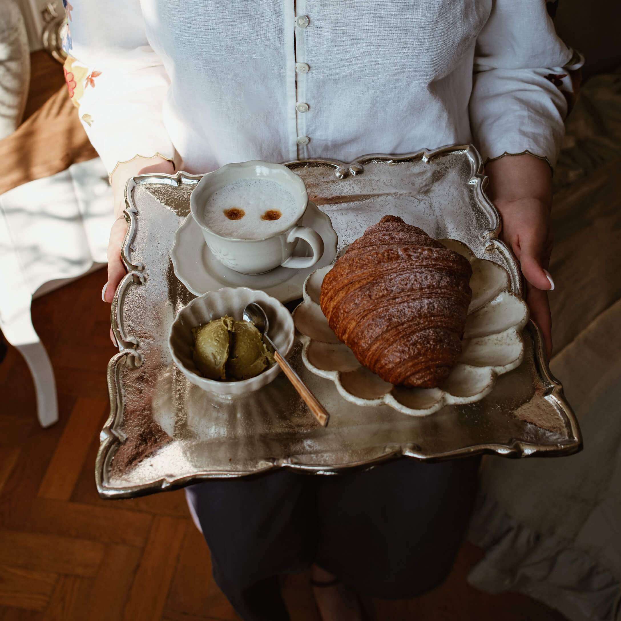 Metalltablett mit Gipfeli, Kaffeetasse und grünem Butteraufstrich auf weissem Porzellan