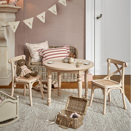 Runder Holztisch mit zwei Stühlen und einem Weidenkorb auf einem Teppich im hellen Kinderzimmer