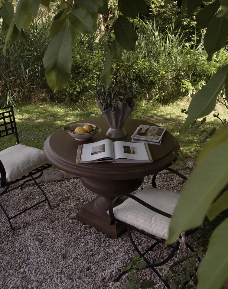 Runder brauner Gartentisch mit Metallstühlen und Polstern auf Kieselstein-Terrasse im grünen Garten