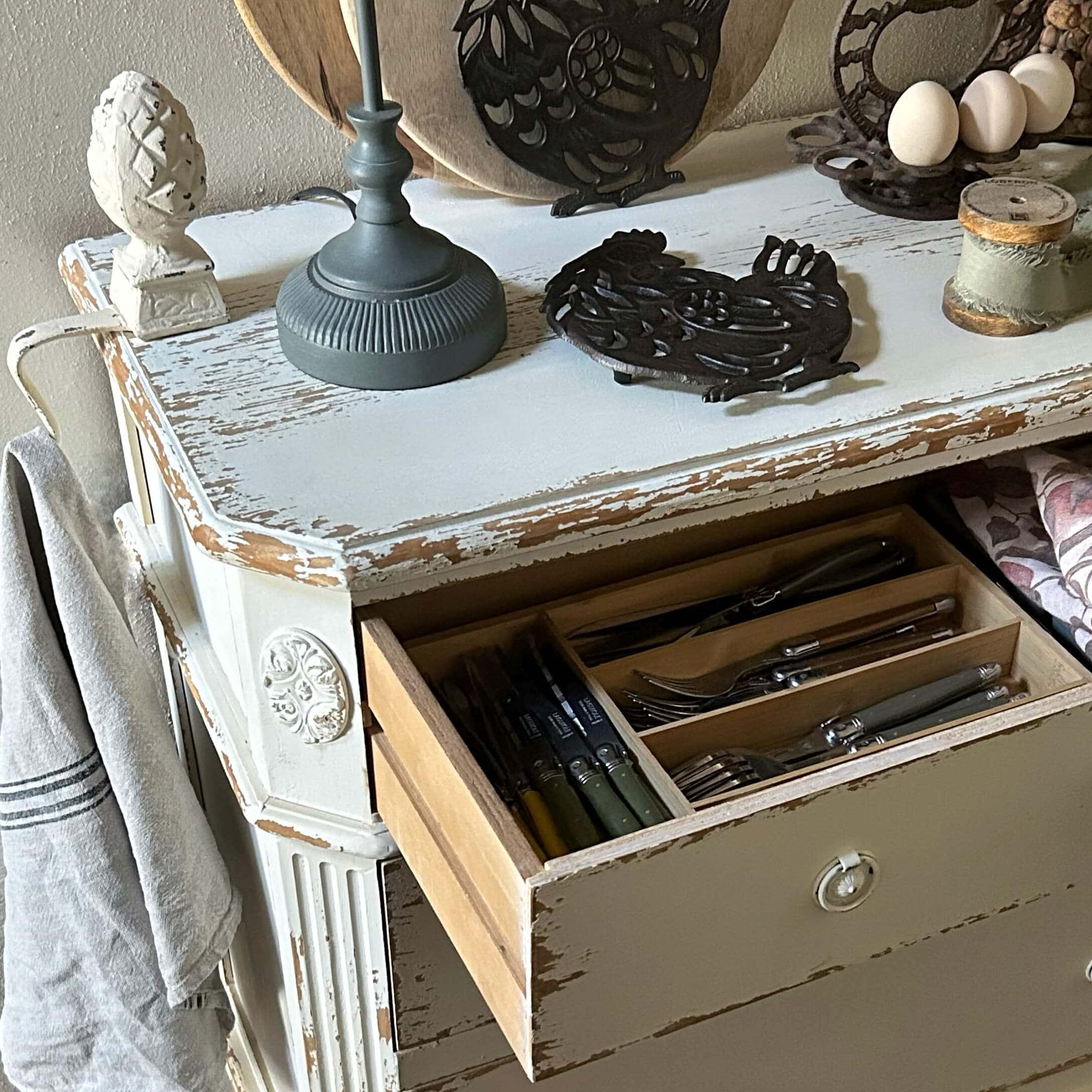 Weisse, im Shabby-Chic-Stil gehaltene Holzkommode mit geöffneter Schublade und Besteck-Organizer