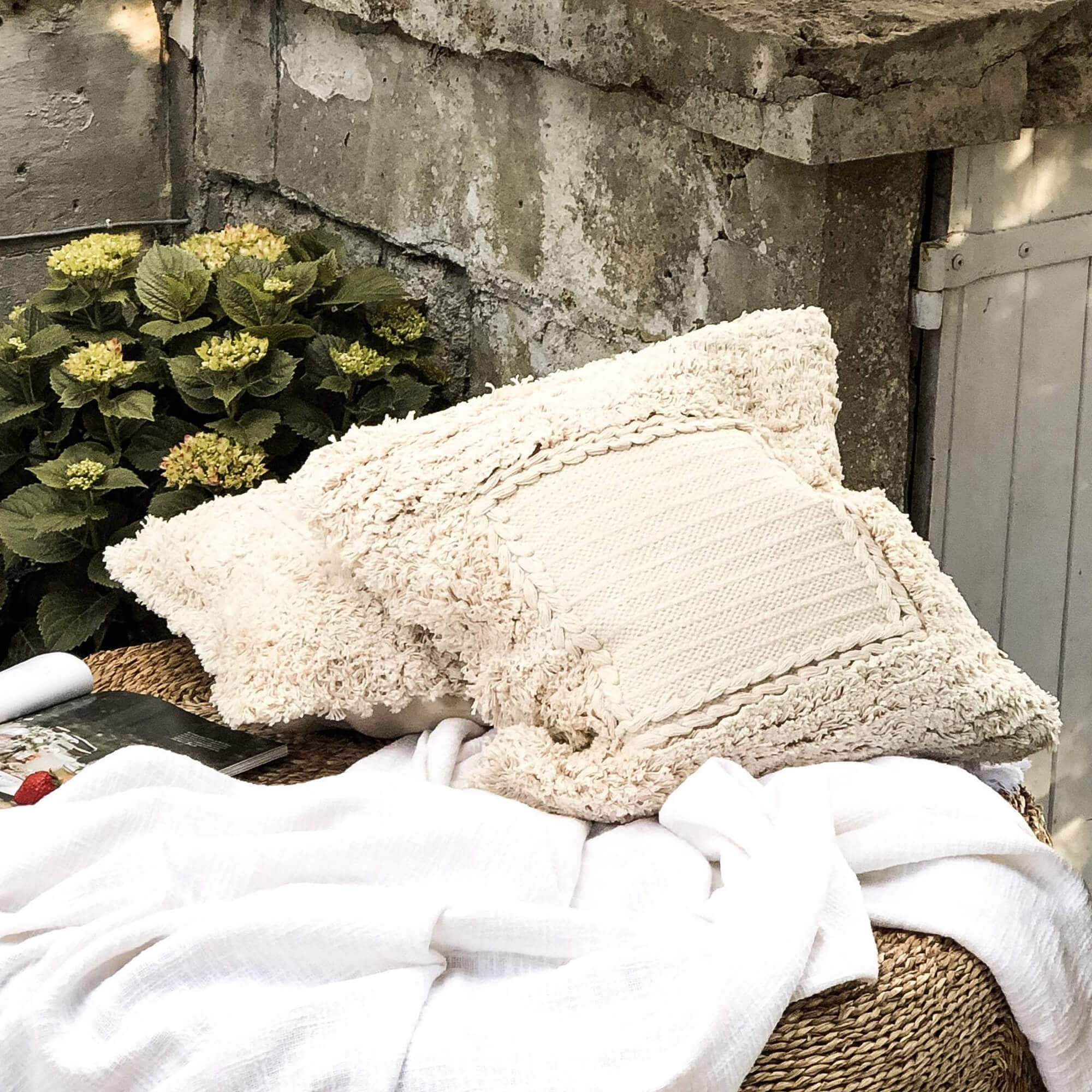 Beige Dekokissen aus weichem Material auf geflochtenem Gartenmöbel mit weisser Decke