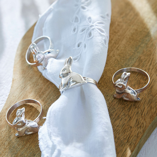 Silberne Ringe mit Hasenmotiv auf weisser Serviette auf Holzbrett, Tischdekoration