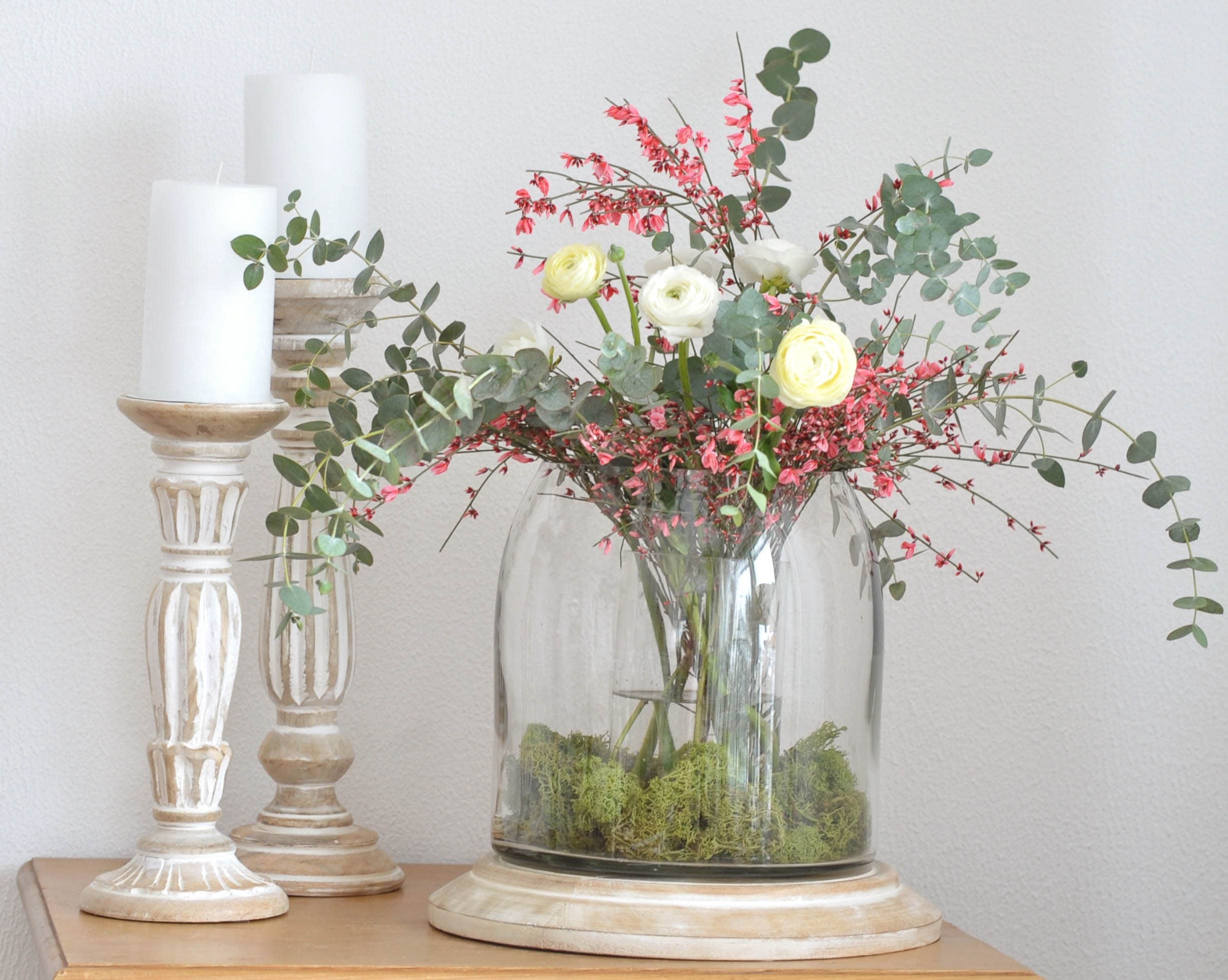Dekorativer Blumenstrauss mit weissen und rosa Blüten in Glasvase auf Holzsockel mit weissen Kerzen