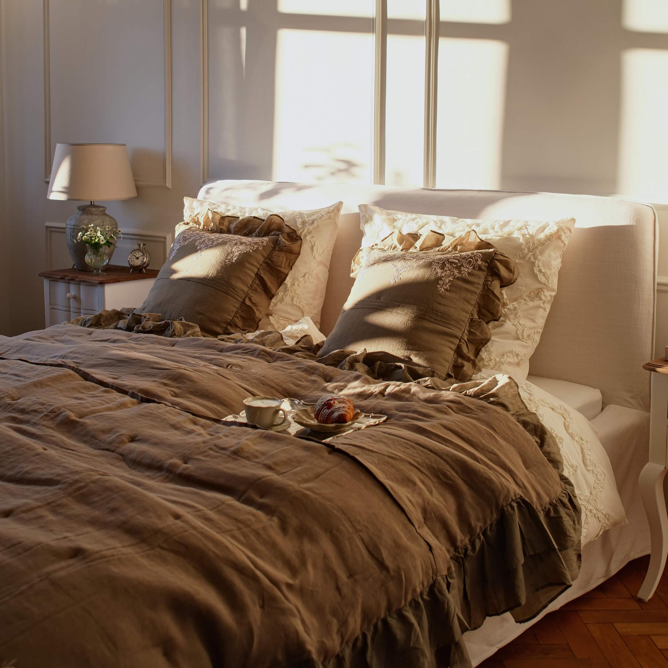 Gemütliches Schlafzimmer mit beiger Leinenbettwäsche und braunen Rüschenkissen im warmen Sonnenlicht