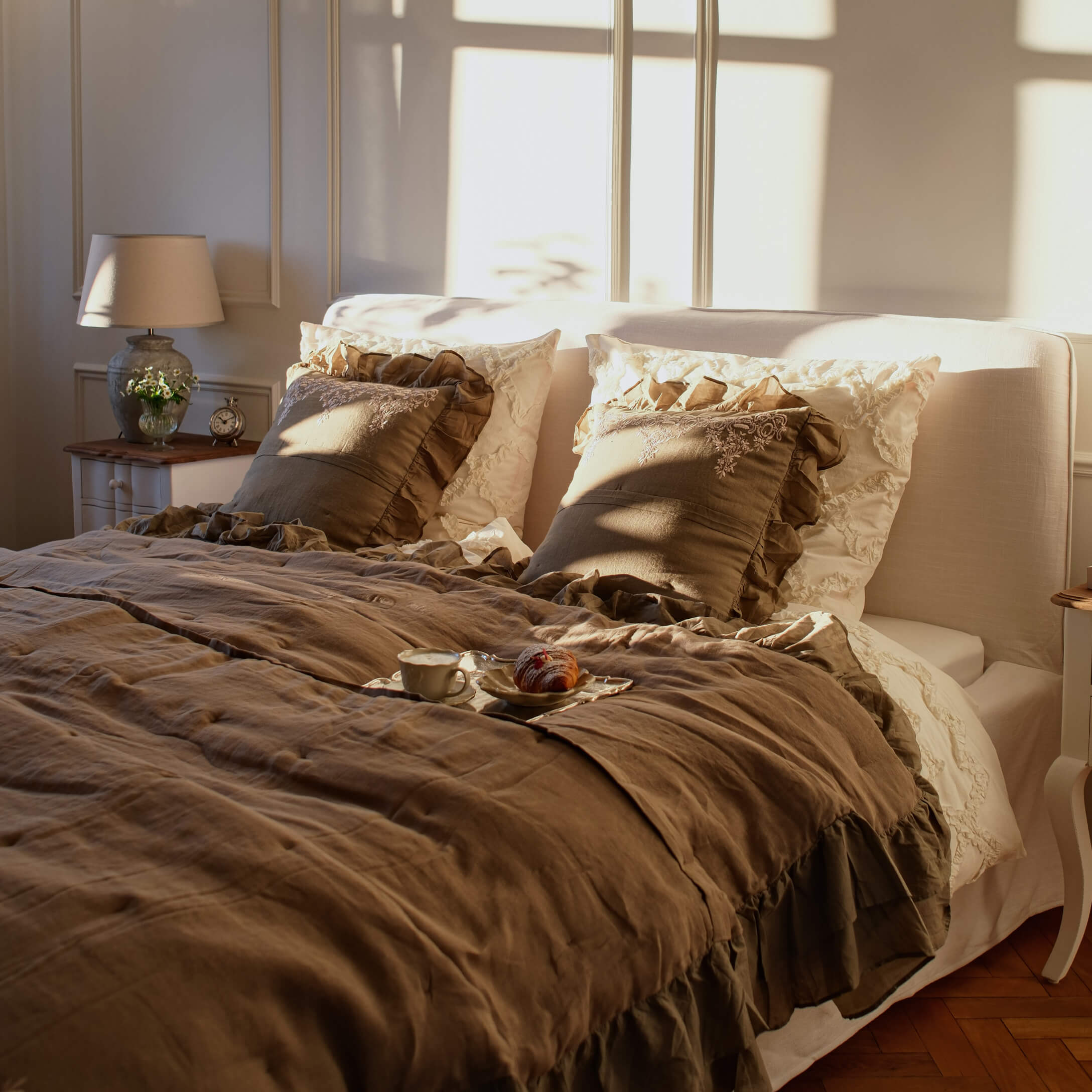 Gemütliches Schlafzimmer mit beiger Leinenbettwäsche und braunen Rüschenkissen im warmen Sonnenlicht