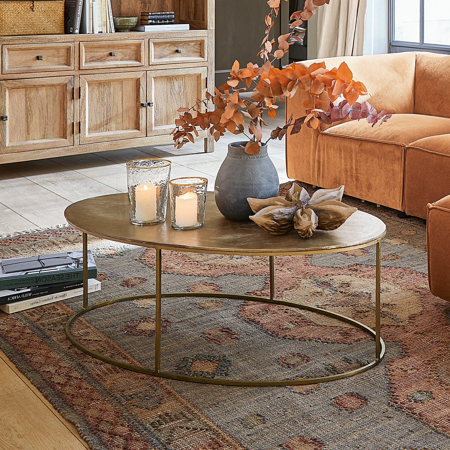 Couchtisch Leron Ovaler Couchtisch mit messingfarbener Metallplatte auf Teppich vor orangefarbenem Sofa im Wohnzimmer