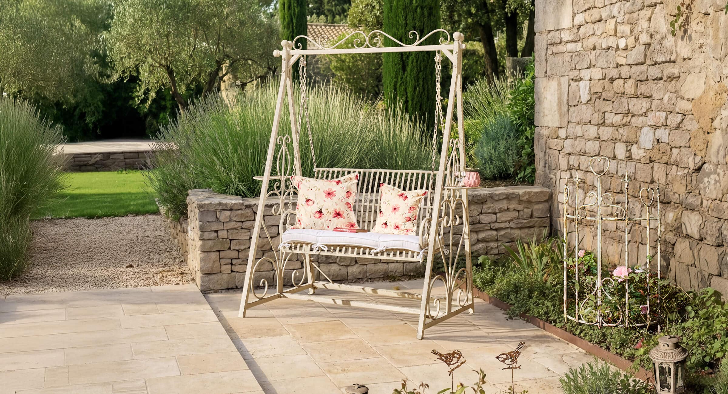 Metall-Gartenschaukel in Creme mit roten Blumen-Kissen auf Stein-Terrasse im Garten