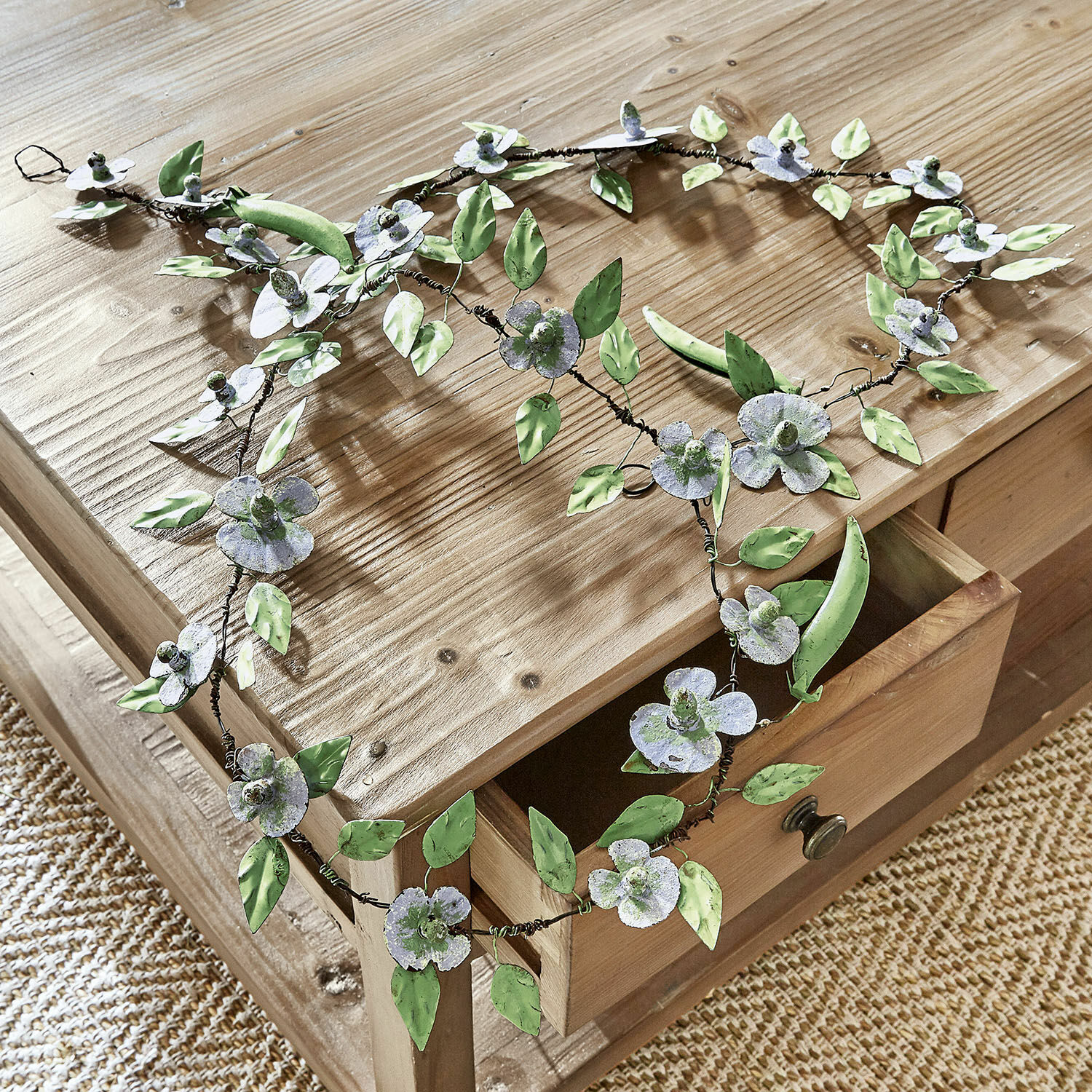 Girlande Cecilia Dekorativer Metallkranz mit grünen und grauen Blüten und Blättern auf hellem Holztisch