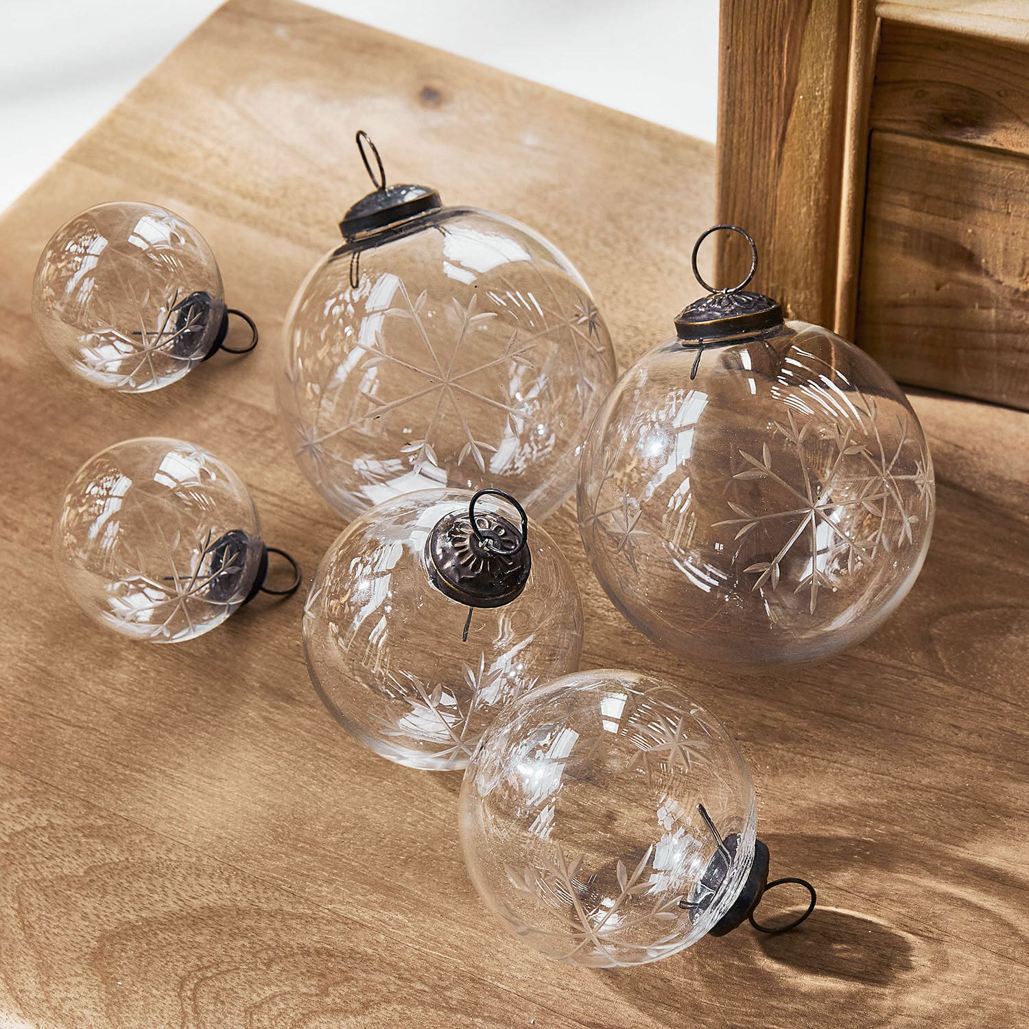 Weihnachtsschmuck 6er Set Coro Set aus transparenten Glas-Weihnachtskugeln mit graviertem Schneeflockenmuster auf Holzunterlage
