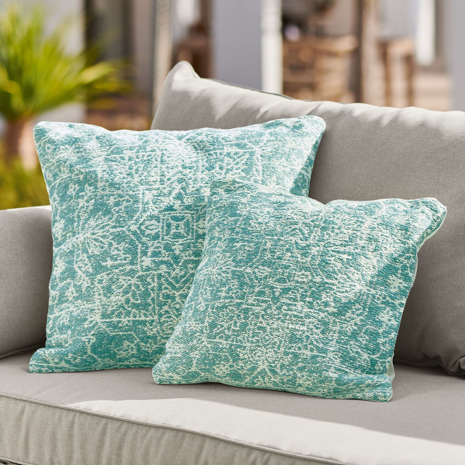 In- & Outdoor-Kissenhülle Bhat Zwei türkis gemusterte Dekokissen auf grauem Sofa, Wohntextilien fürs Wohnzimmer