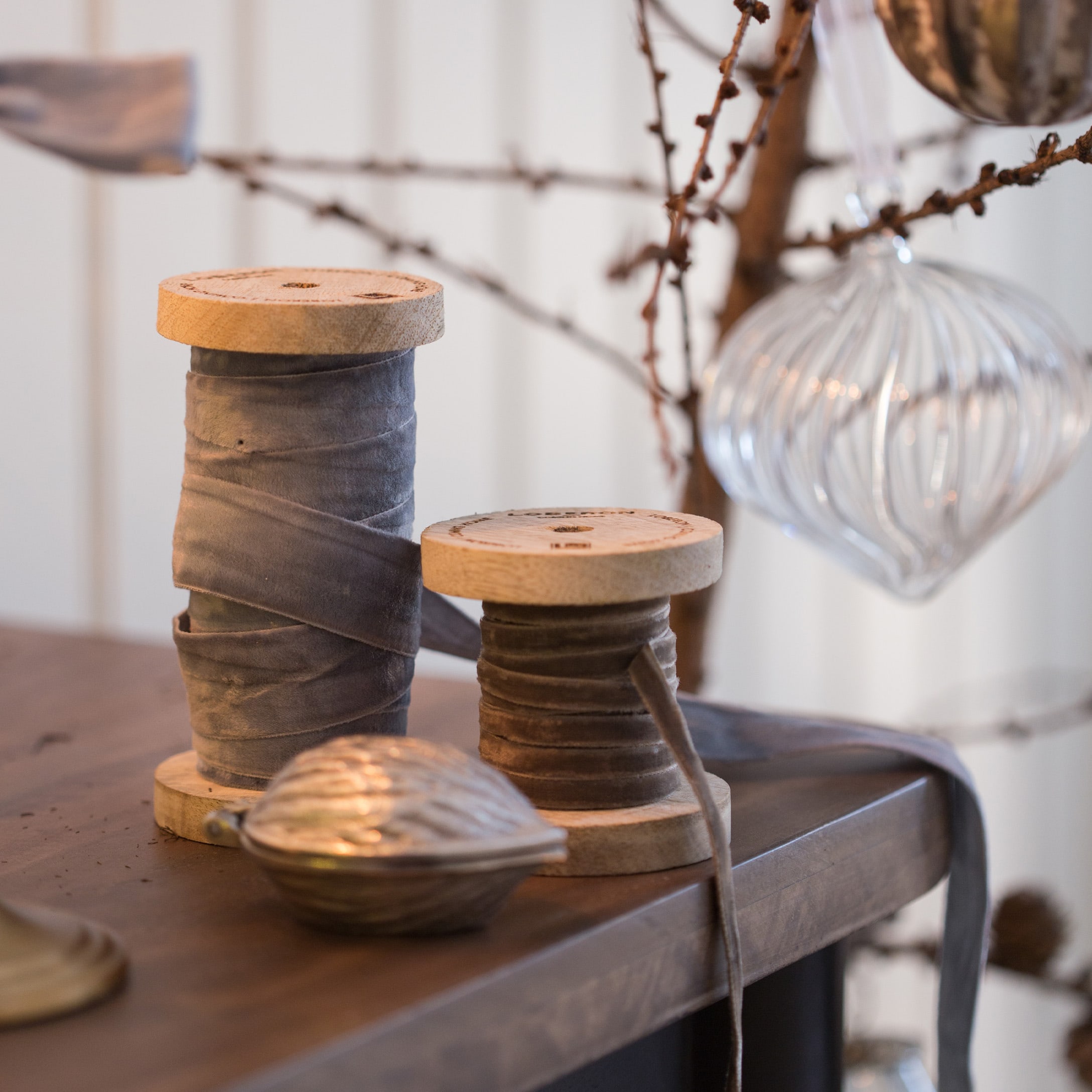 Holzspulen mit grauem Samtband auf Holztisch neben Weihnachtsdekoration aus Glas