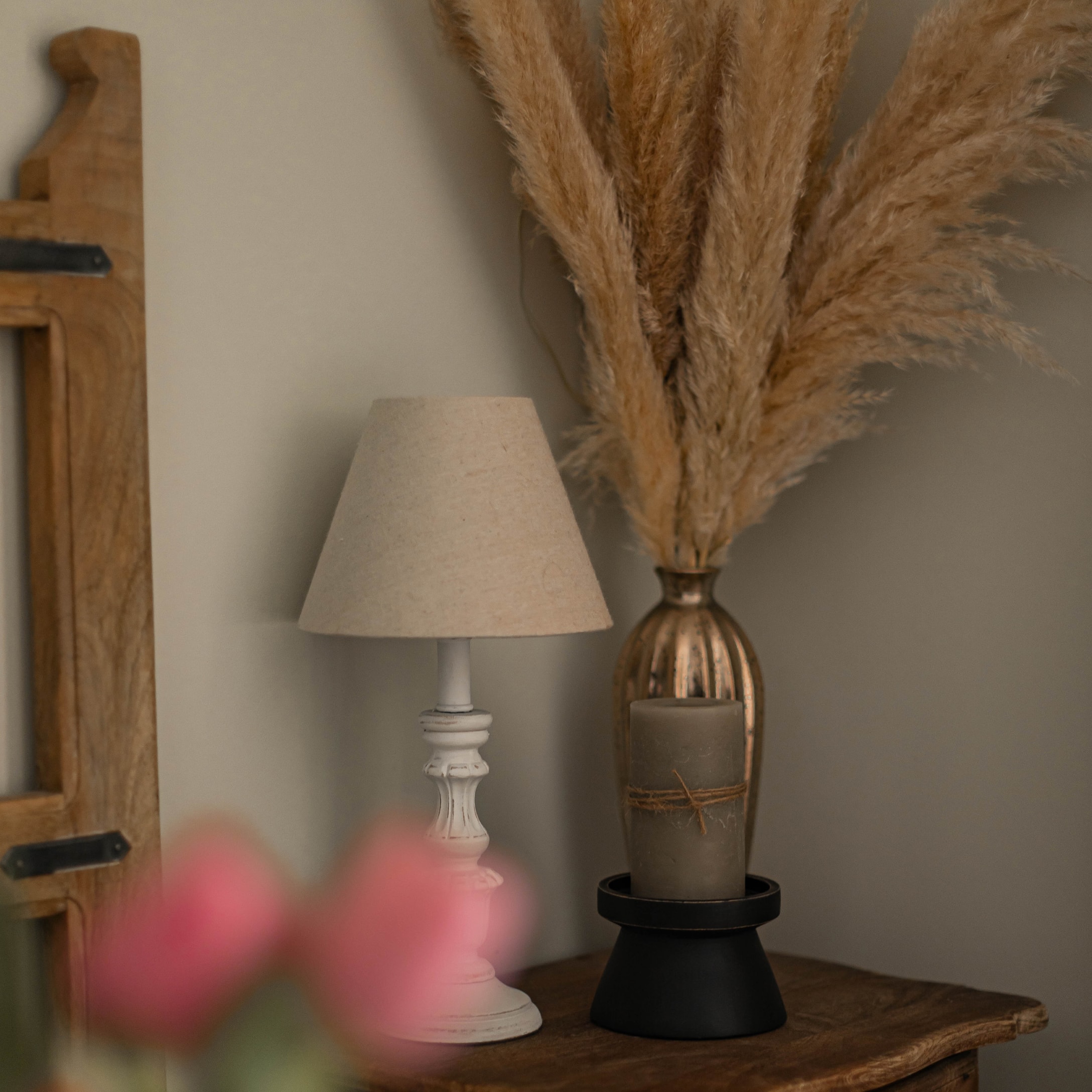 Weisse Holztischlampe mit beigem Lampenschirm und getrockneten Gräsern als Dekoration auf Holztisch