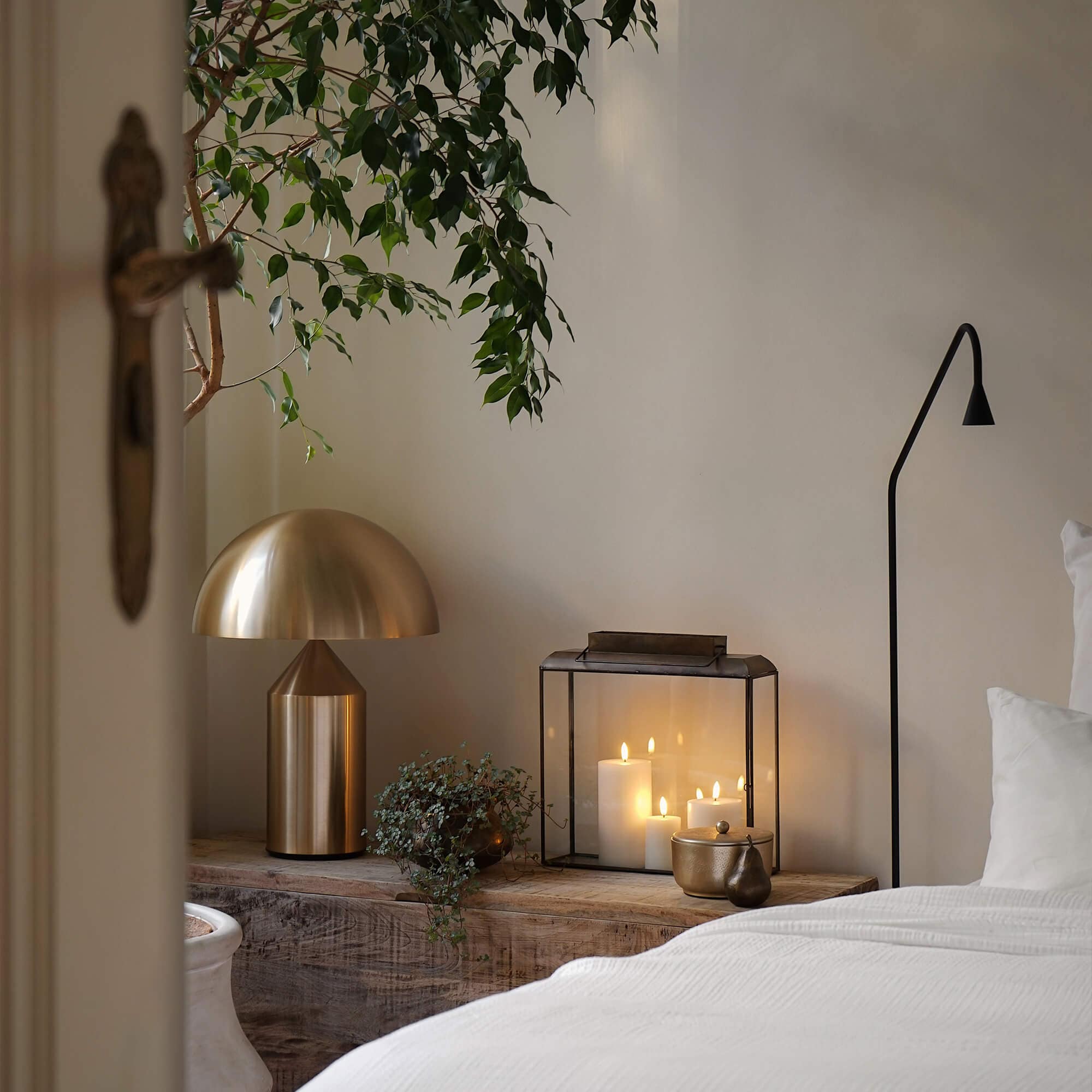 Goldene Metall-Tischlampe und Glaslaterne mit weissen Kerzen auf Holzablage im Schlafzimmer