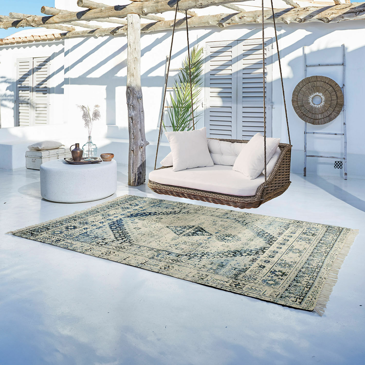 In- & Outdoor-Teppich Daly Vintage Teppich in Beige und Blau auf hellem Boden neben Rattan-Hängesofa mit weissen Kissen