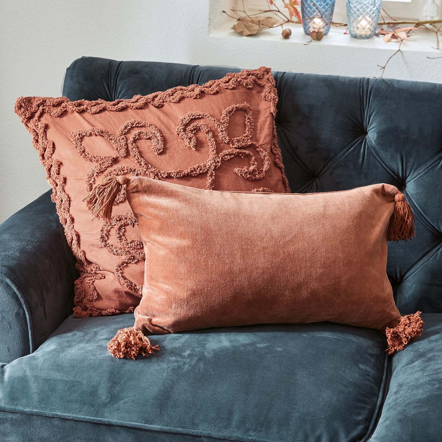 Zwei dekorative Kissen aus orangefarbenem Samt auf dunkelblauem Sofa, weiche und stilvolle Wohnaccessoires