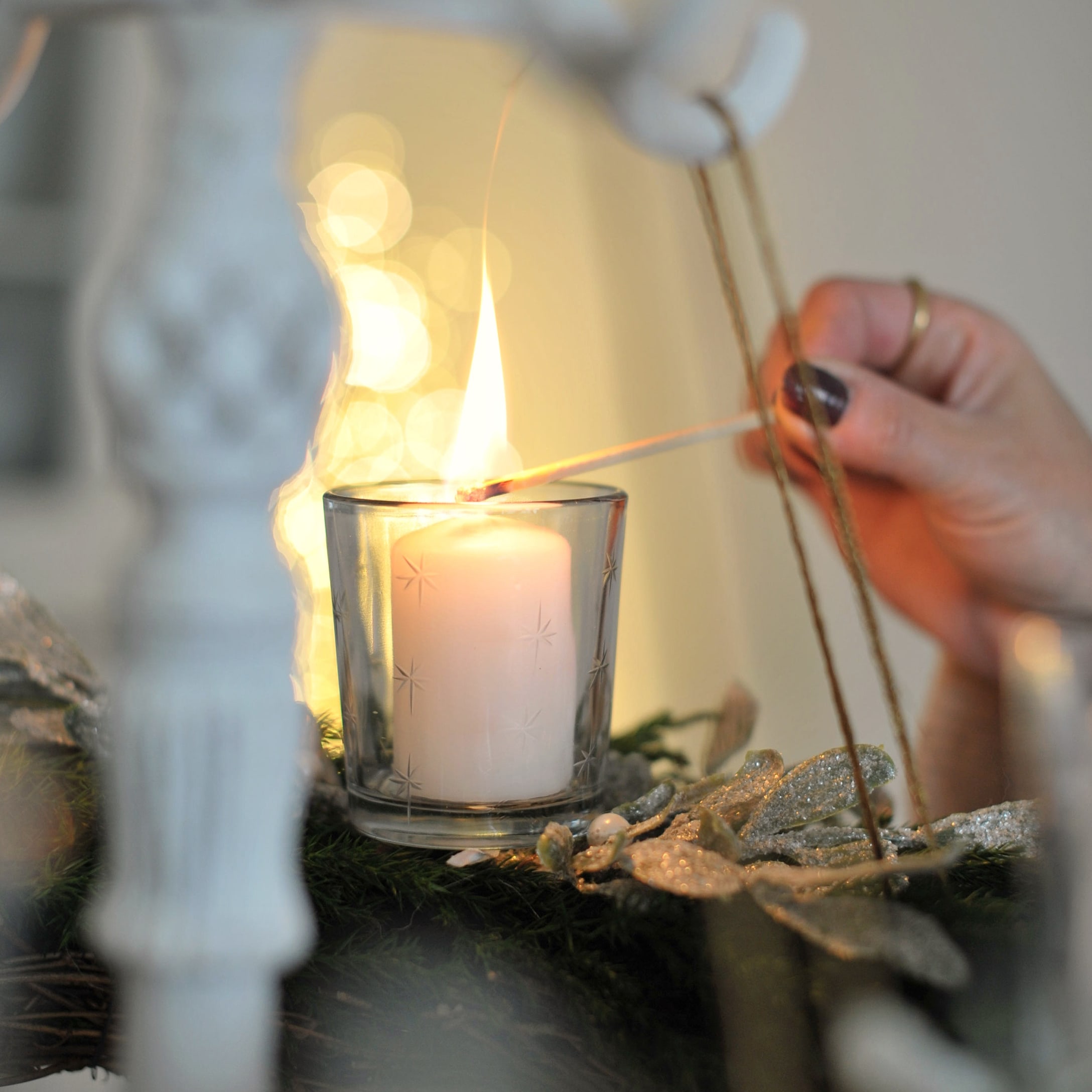 Weisse Kerze im Glaswindlicht auf grünem Adventskranz mit glitzernder Dekoration