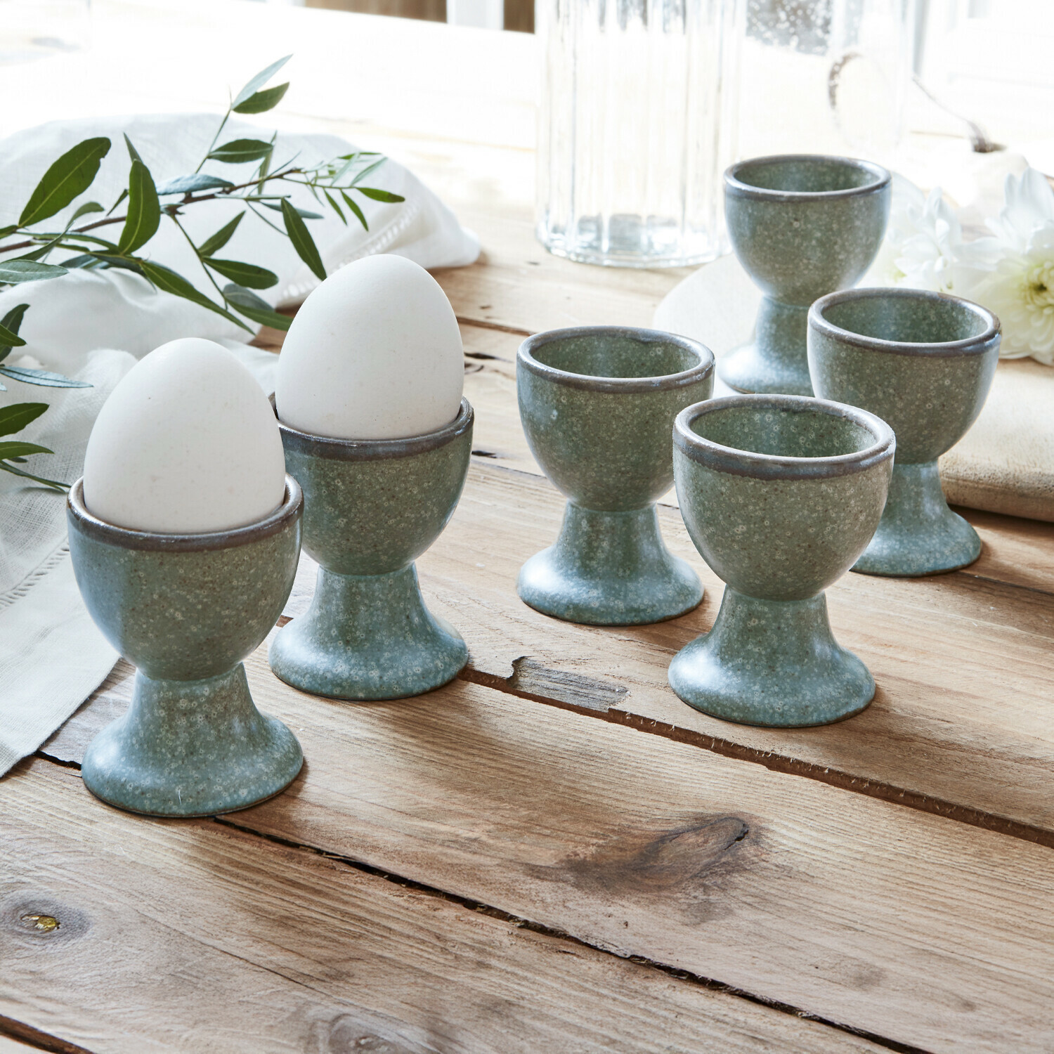 Set aus sechs grünen Keramik-Eierbechern auf Holztisch für die Küche