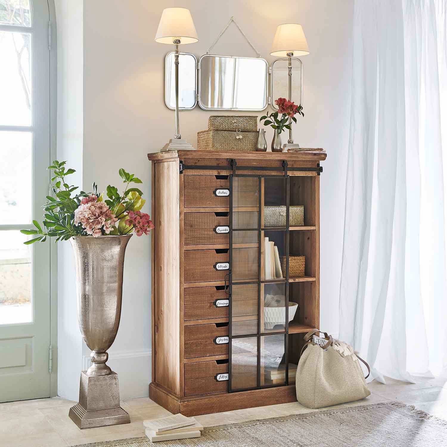 Holzkommode mit Schubladen und Glastür in hellem Raum mit Dekoration und Lampen