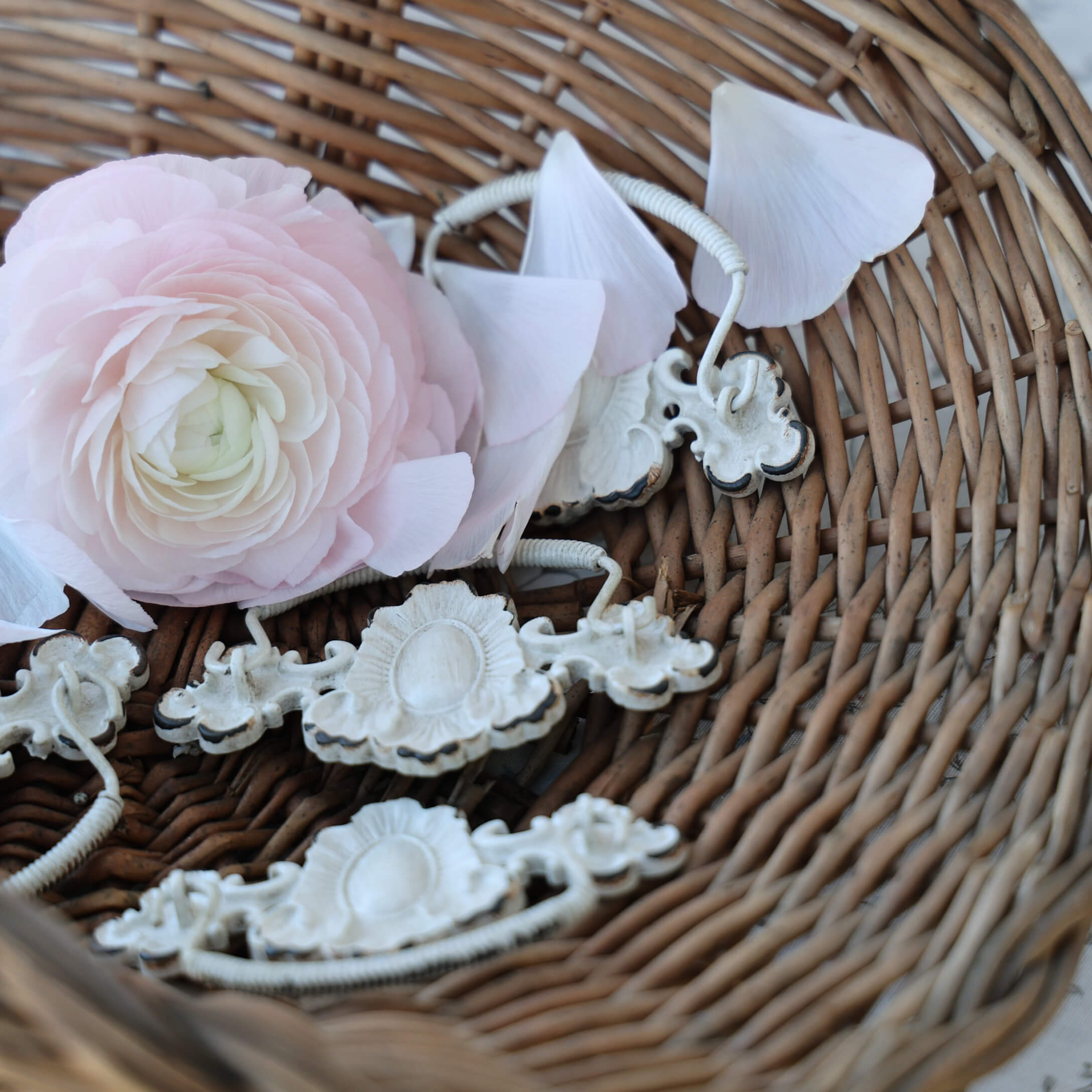 Zarte rosa Blume und weisse Metallgriffe in einem Weidenkorb, Vintage-Innendekoration
